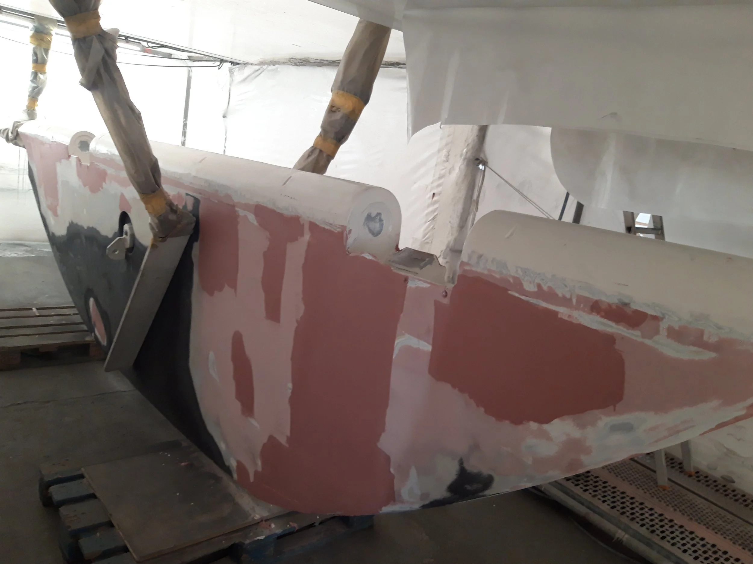 A boat is being prepared for painting or repair, with parts covered in primer and paint, and protected with masking tape.