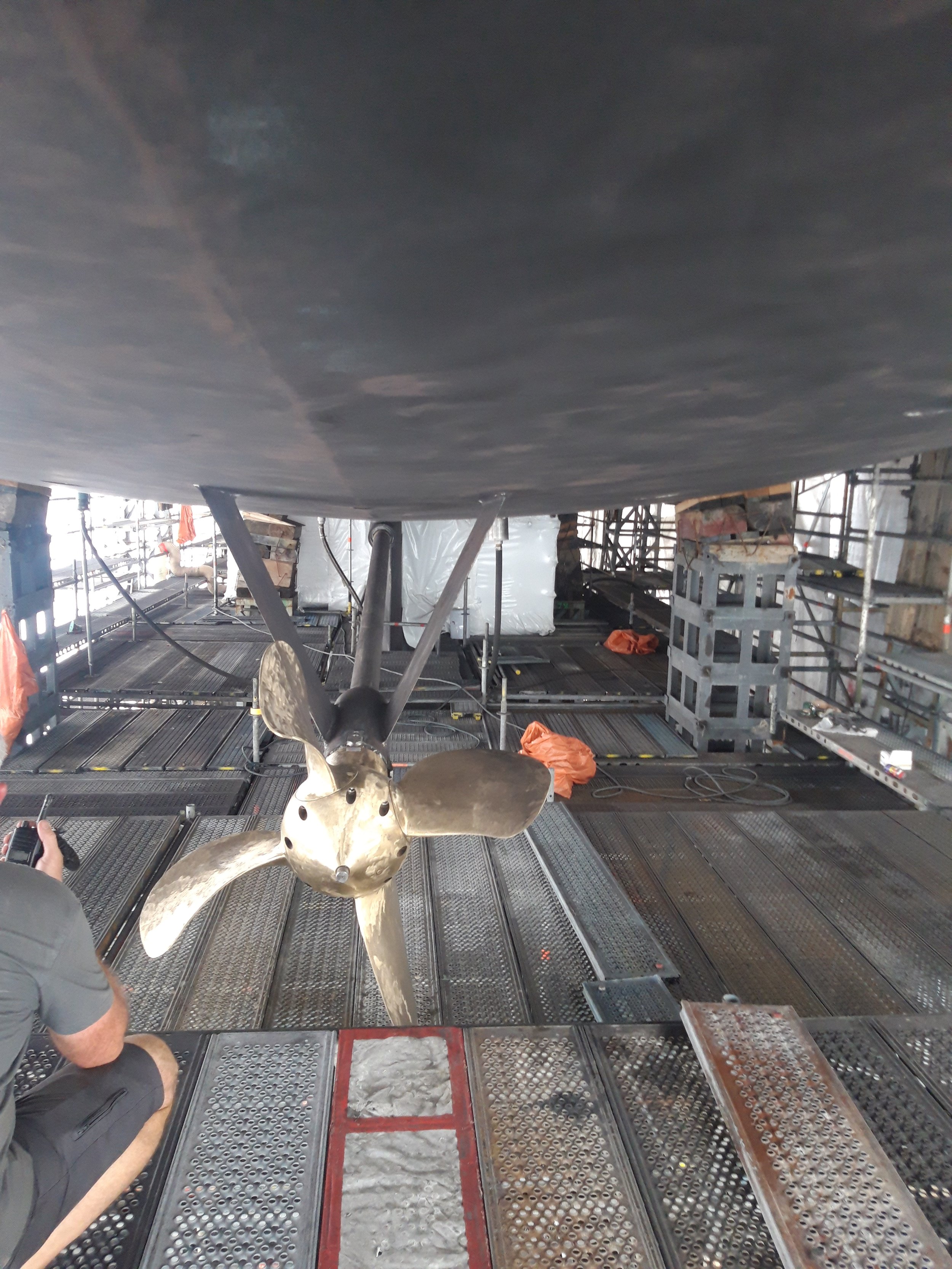 Inside view of a maritime vessel's propeller and underside, showing the metal structure and scaffolding around the machinery.