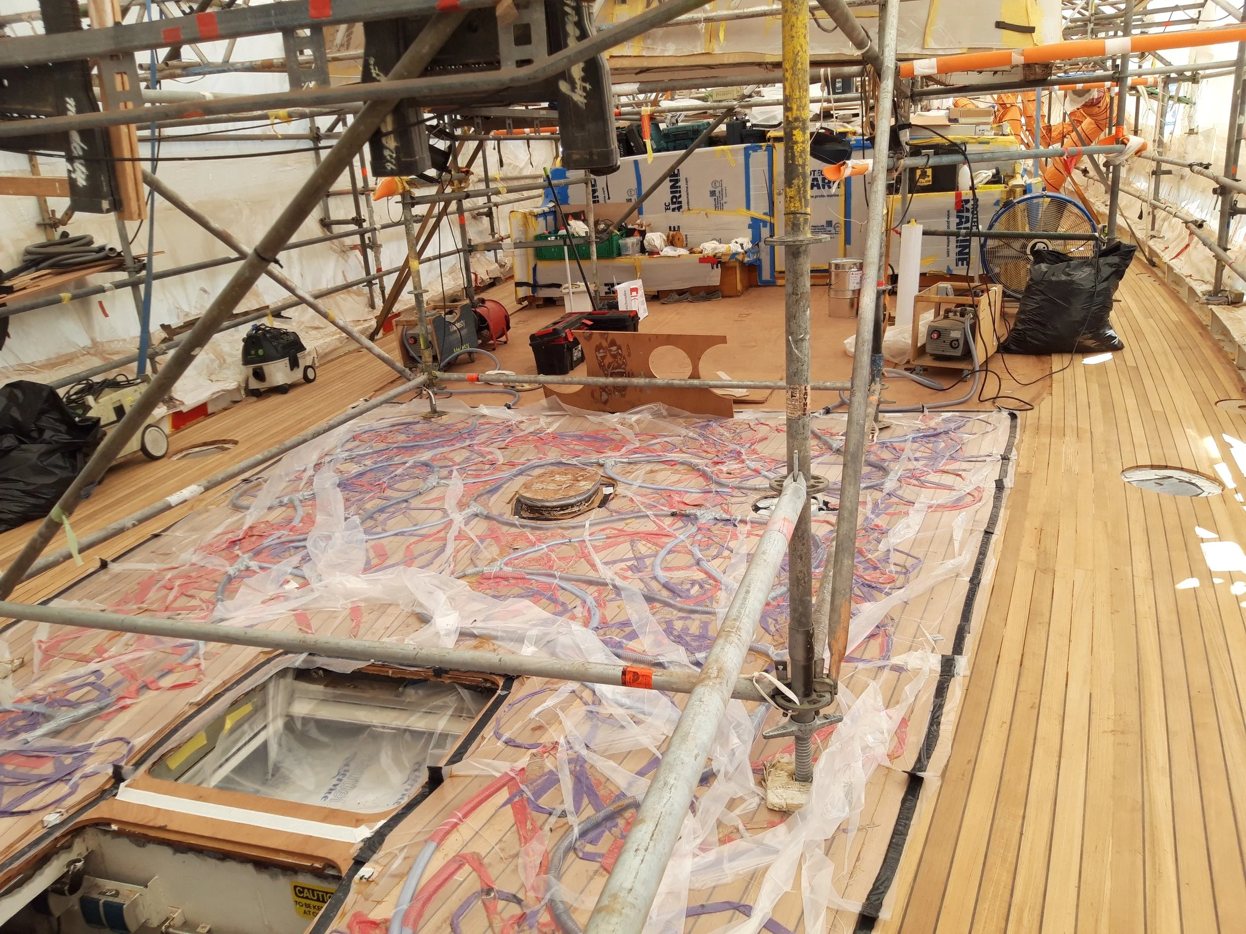 Under construction on a boat deck, showing scaffolding, electrical wiring, and tools with a wooden deck.