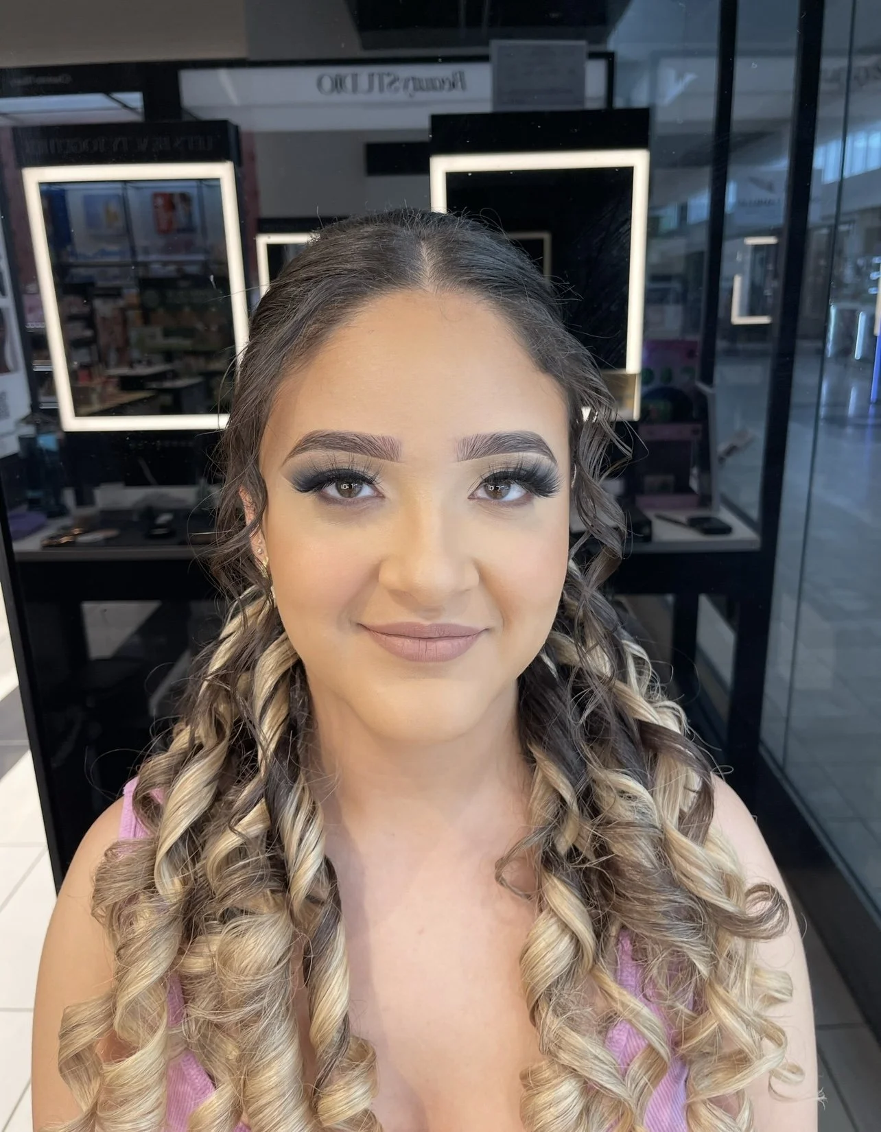 A woman with curly blonde hair and makeup, sitting in a salon.