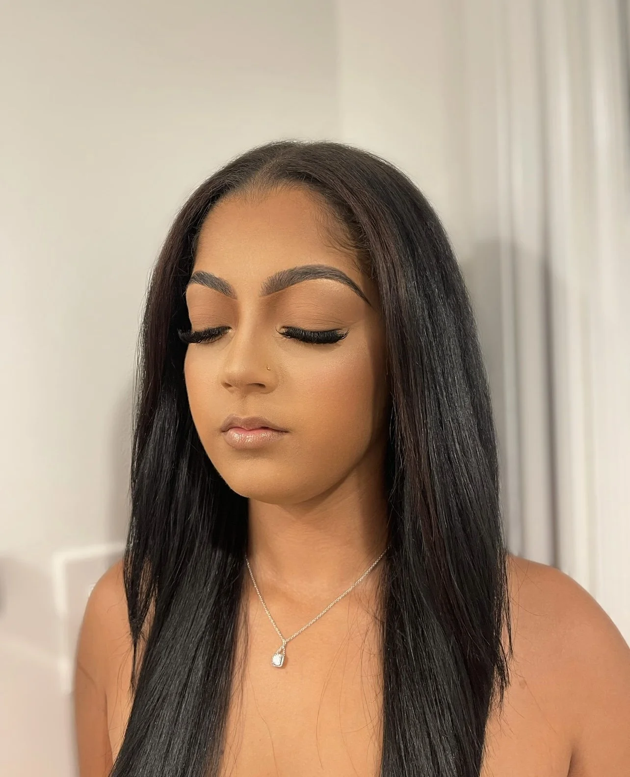 Close-up portrait of a woman with closed eyes, long dark hair, and a silver necklace with a gemstone pendant.