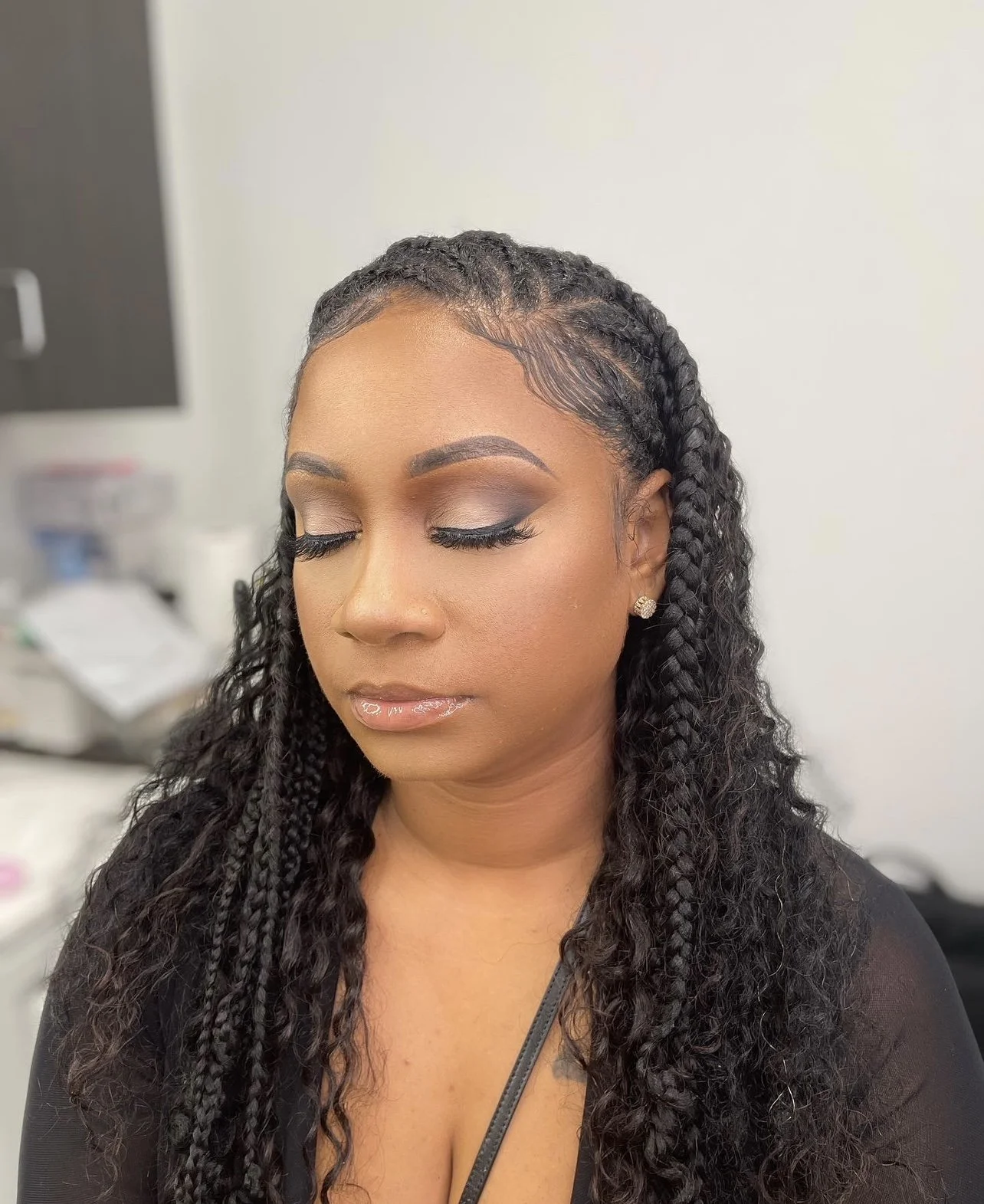 A woman with long, curly, braided hair and makeup, including eyeshadow and glossy lips, with her eyes closed.