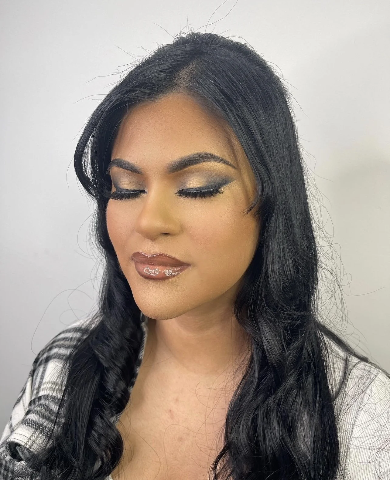 A woman with long black hair, closed eyes, and makeup including eye shadow, eyeliner, and glossy lipstick.