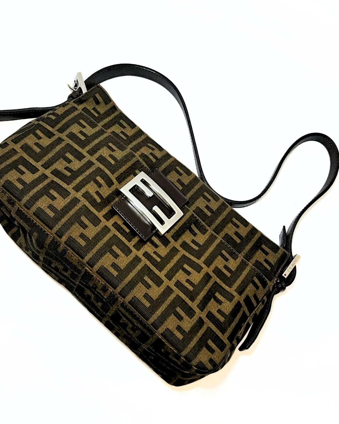 Designer handbag with black straps and a patterned fabric featuring the Fendi logo in black and brown, with a metal buckle detail on the front.