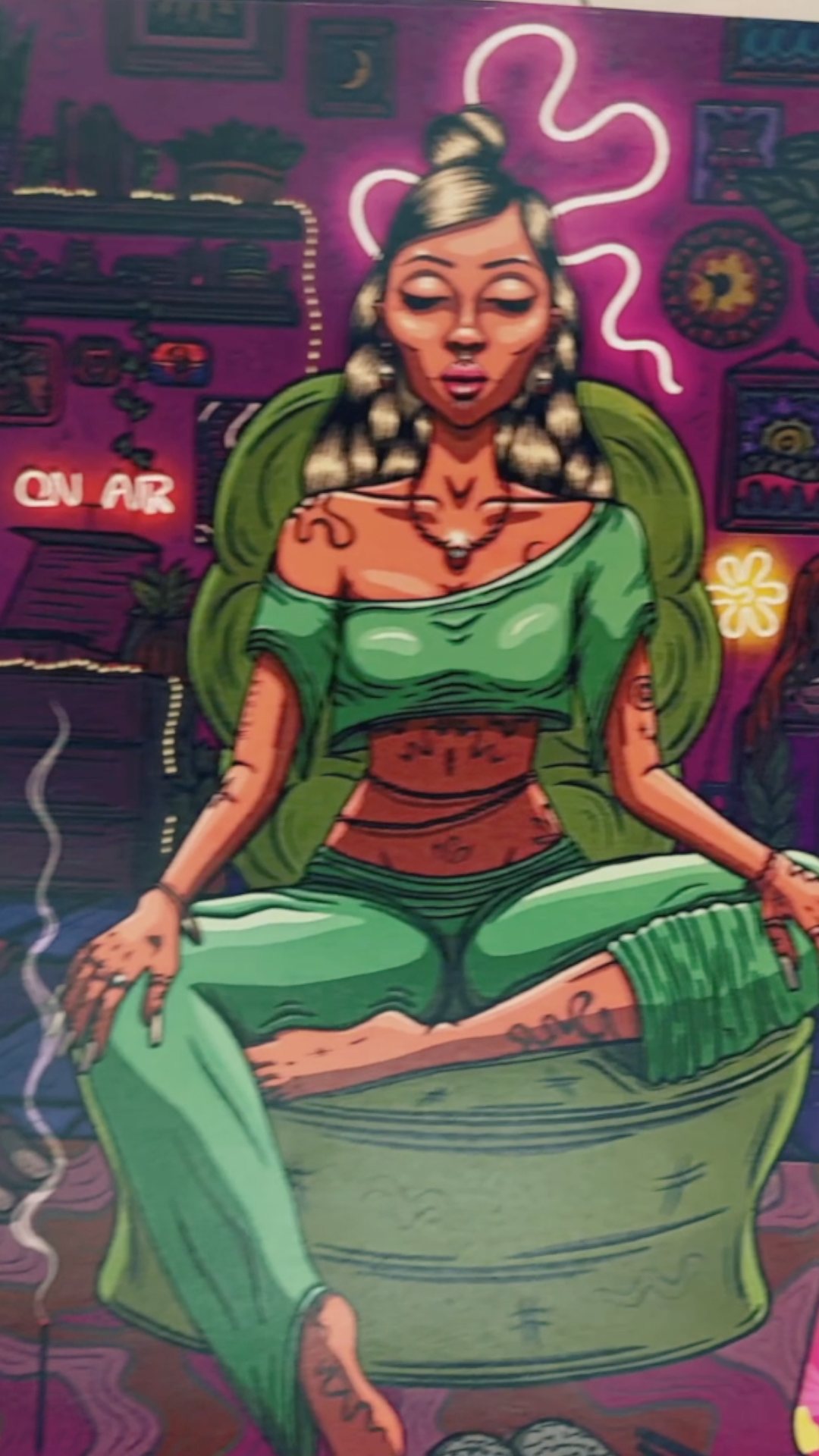 A woman with tattoos, wearing a green off-shoulder top and green pants, sits cross-legged in a colorful room with neon lights, plants, and artwork on the walls, and a neon 