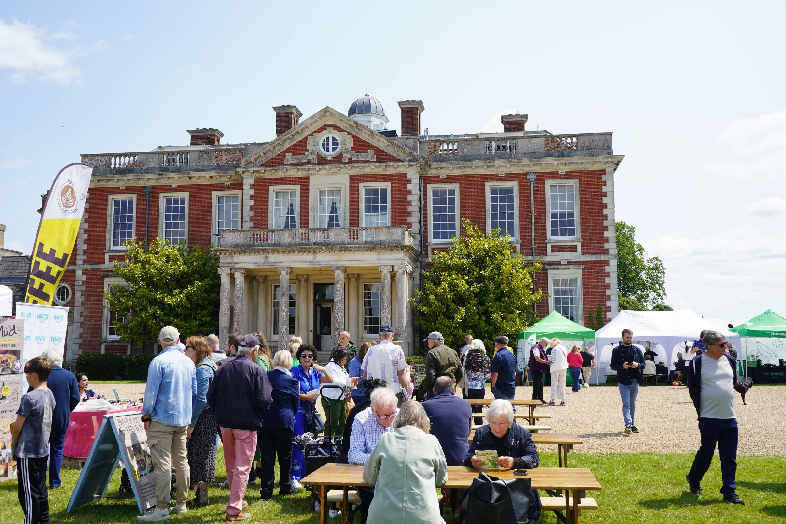 People attending outdoor event in front of a large historic red brick building with columns