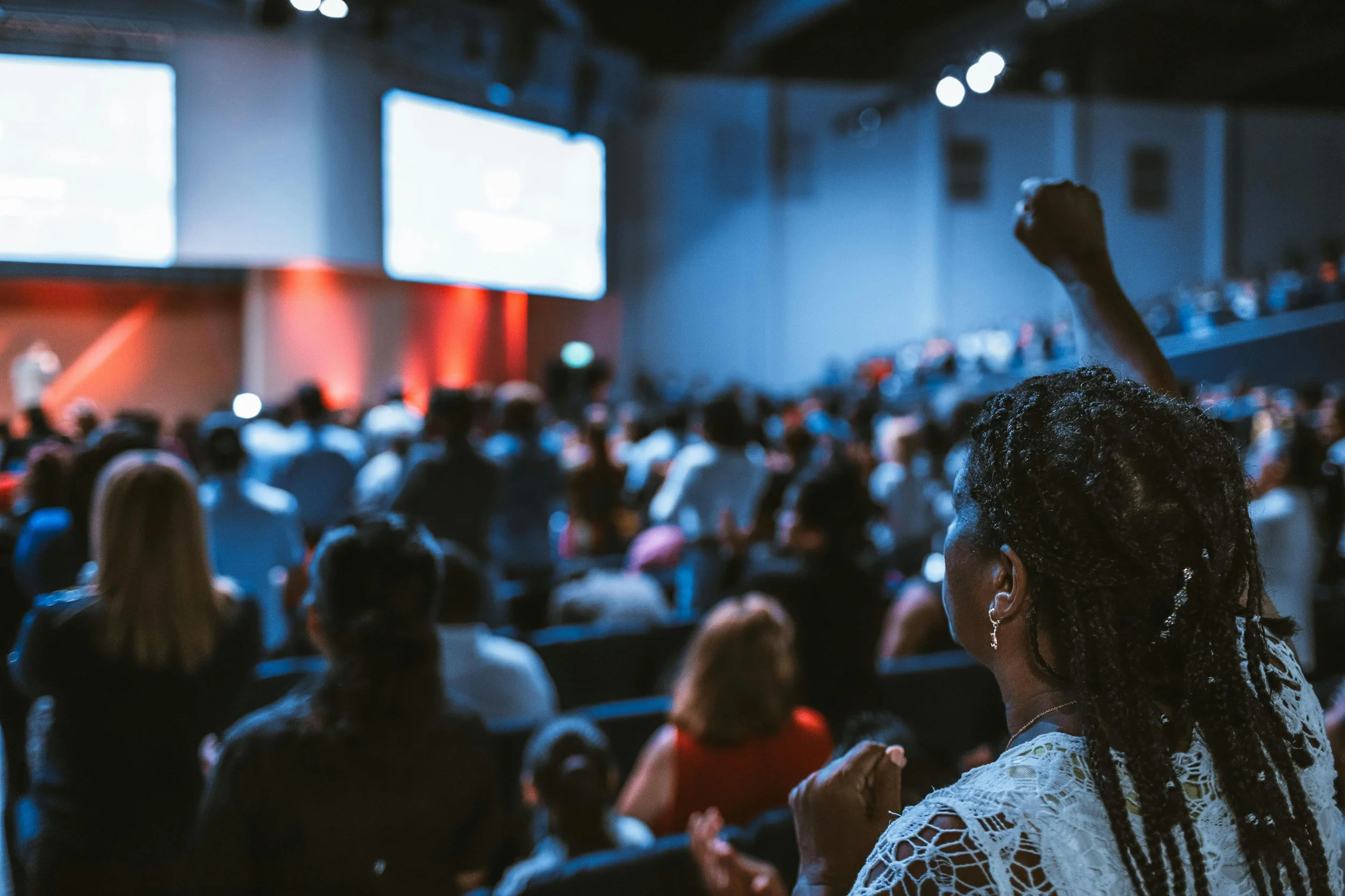 A large crowd of people attending a conference or event in an auditorium, with many facing a stage or screen at the front.