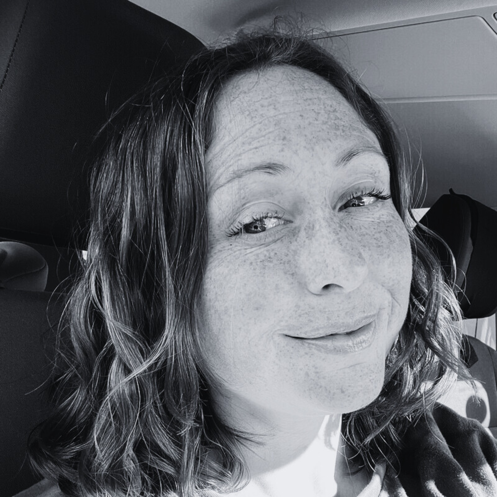 A woman with curly hair and freckles smiling in a black and white photo.