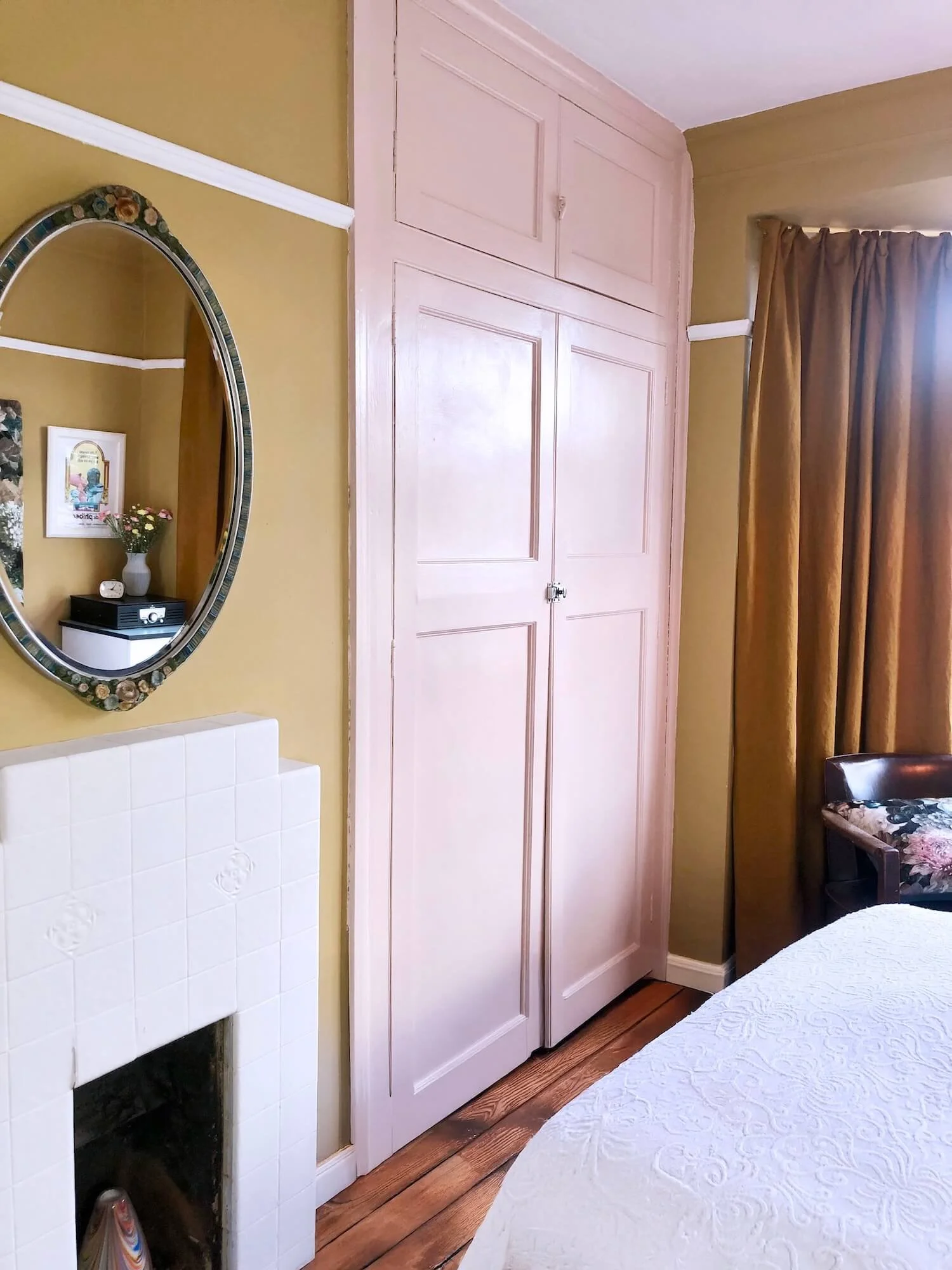 Bedroom with painted built-in wardrobe, oval mirror and warm gold curtains