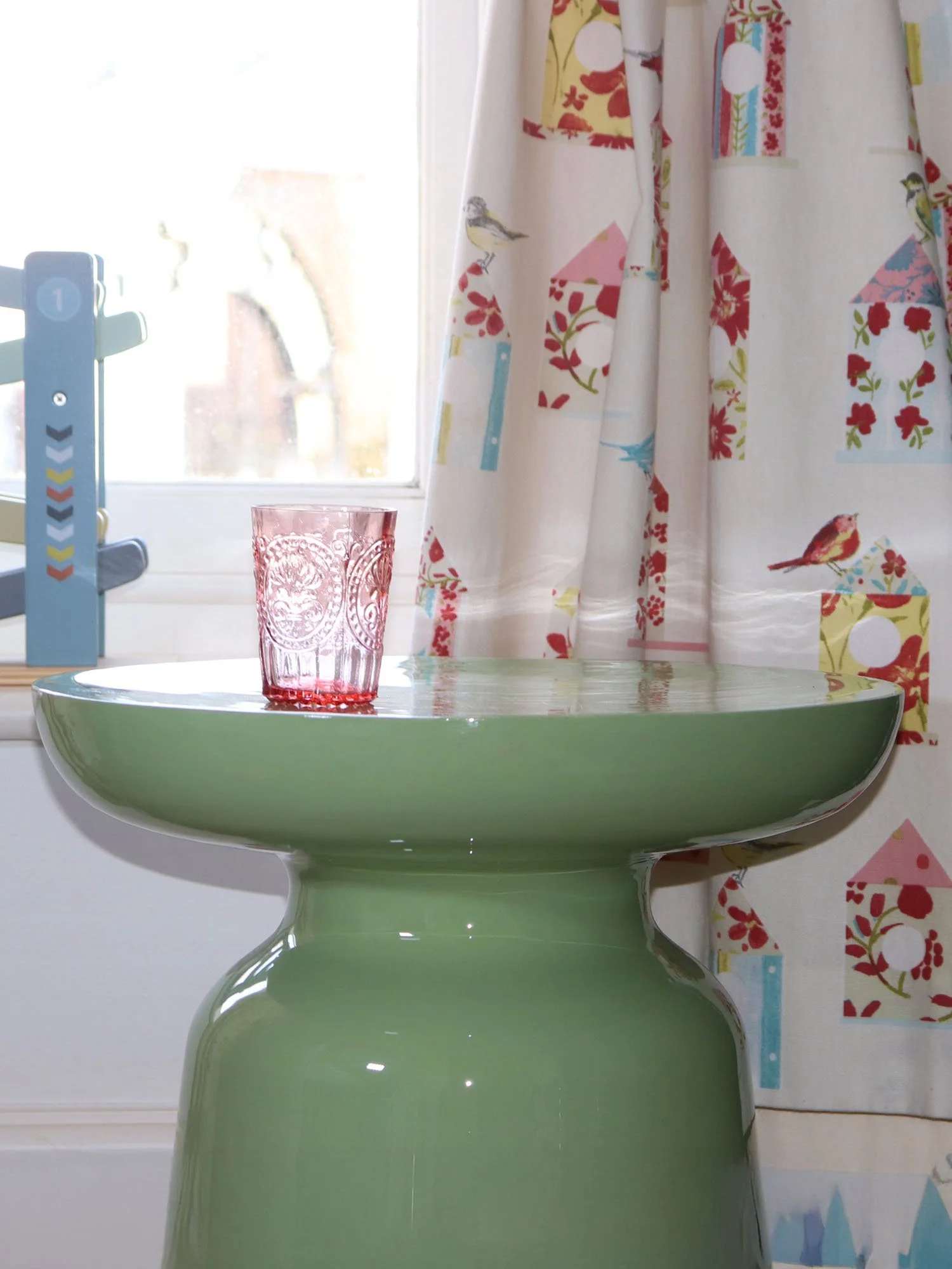 Close-up of matcha green metal side table with pink glass tumbler