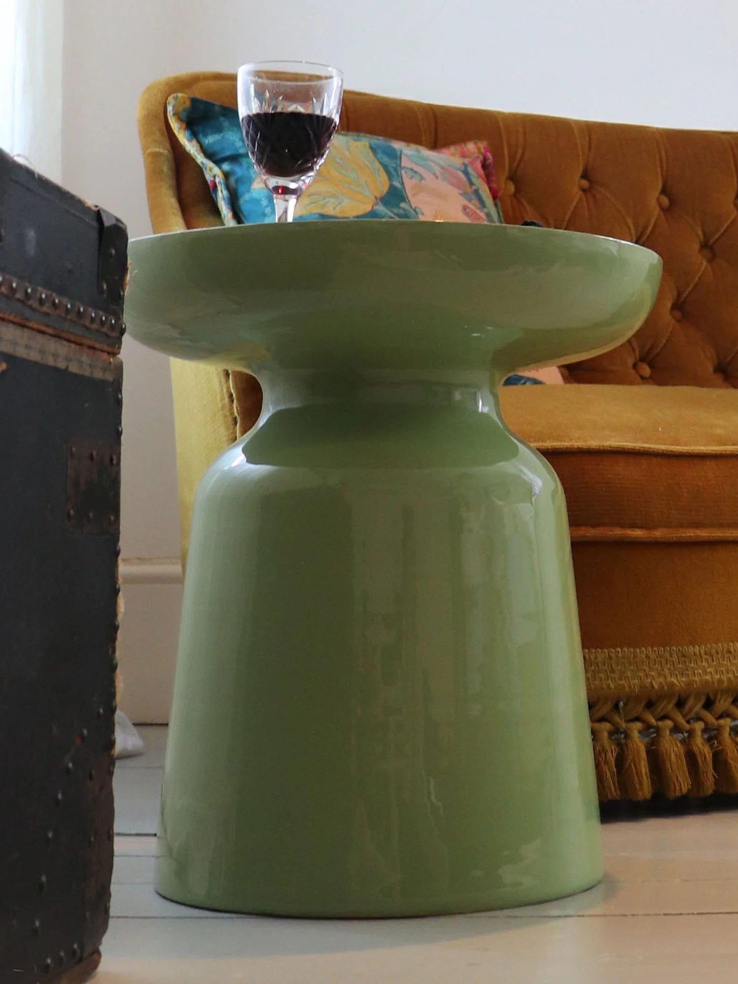 Matcha green side table with wine glass beside mustard sofa and floral cushion
