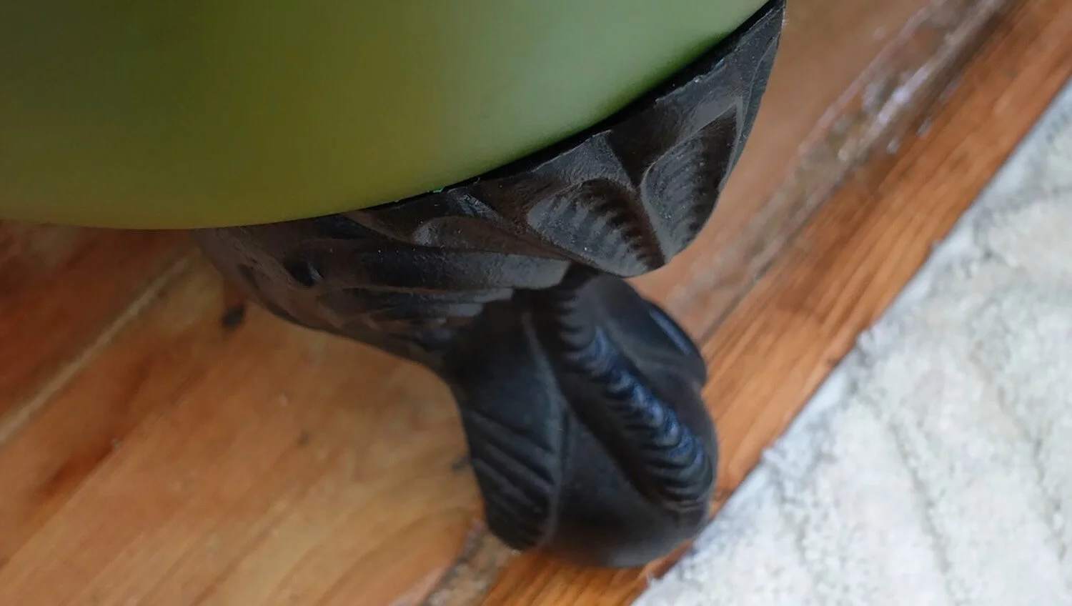 Close-up of green roll-top bath and wooden flooring