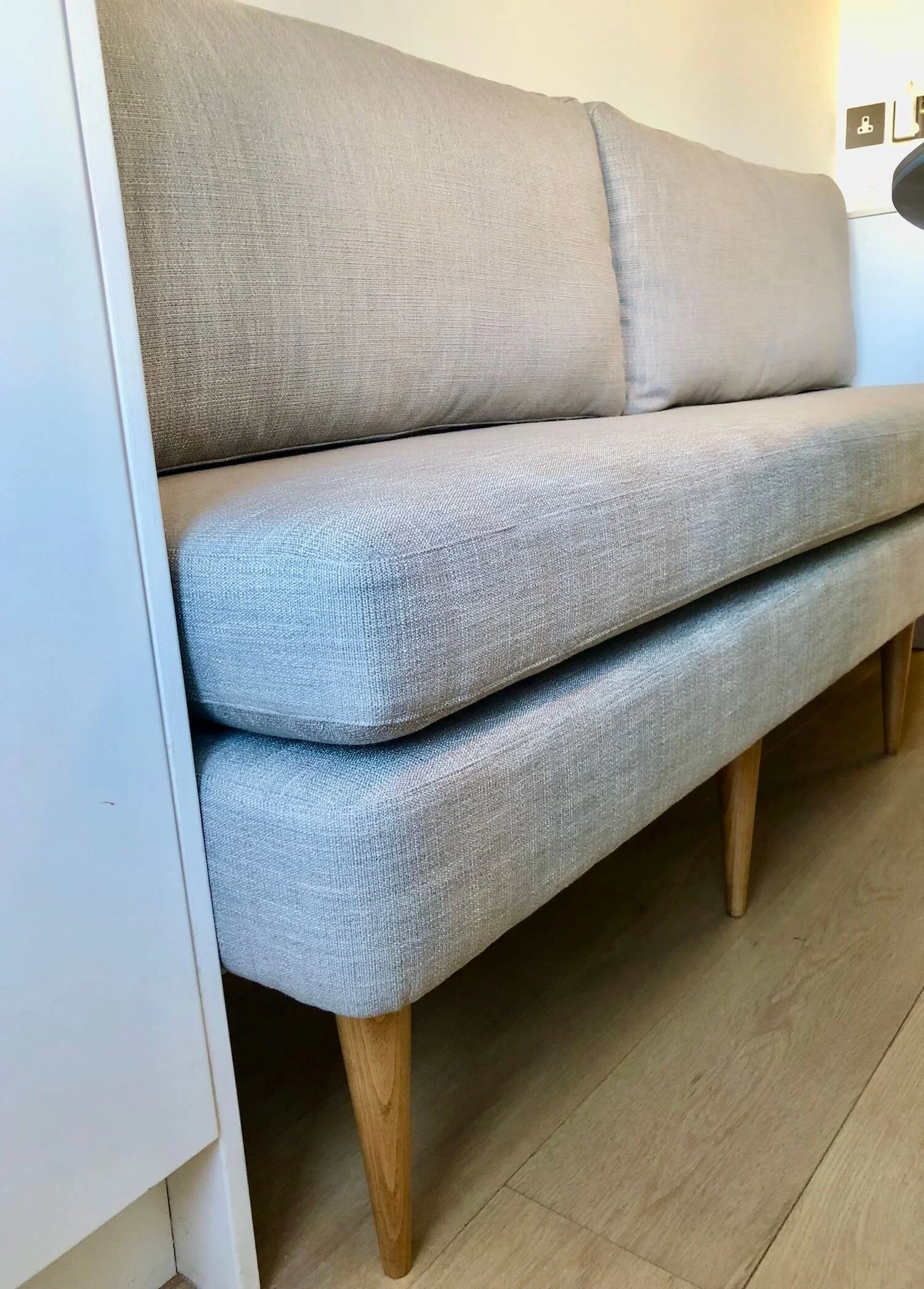 Light grey upholstered banquette with deep cushions and wooden legs