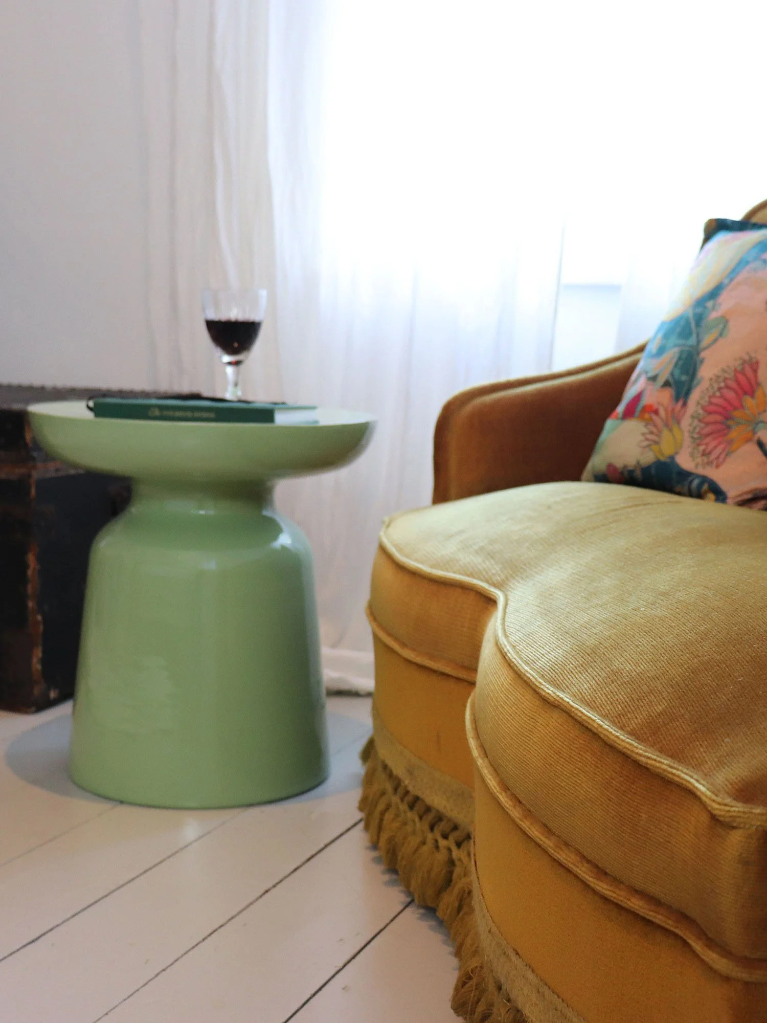 Matcha green metal side table with wine glass next to mustard armchair