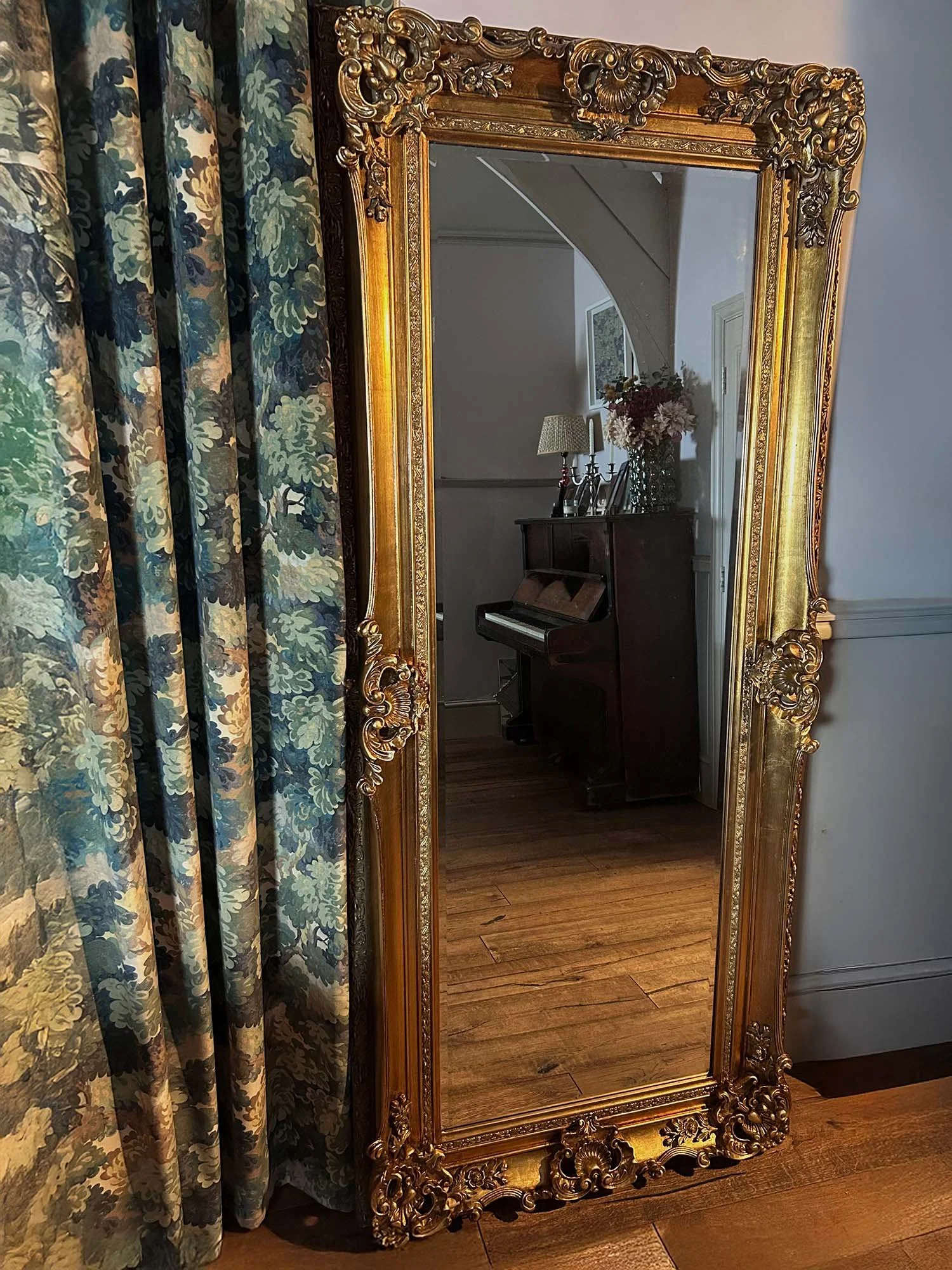 Antique gold tall regal mirror beside patterned curtains in interior room