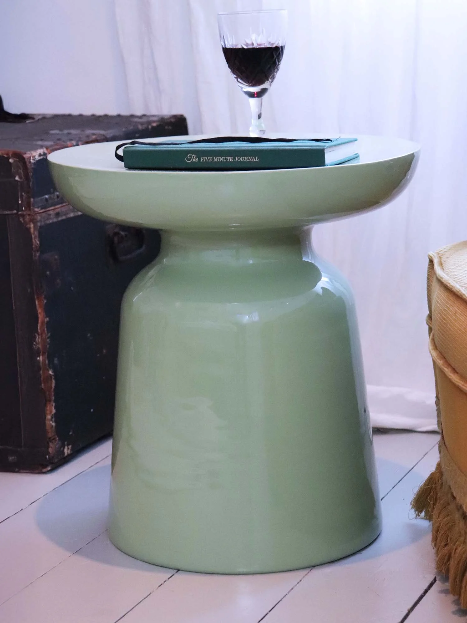 Matcha green metal side table with wine glass beside dark vintage trunk