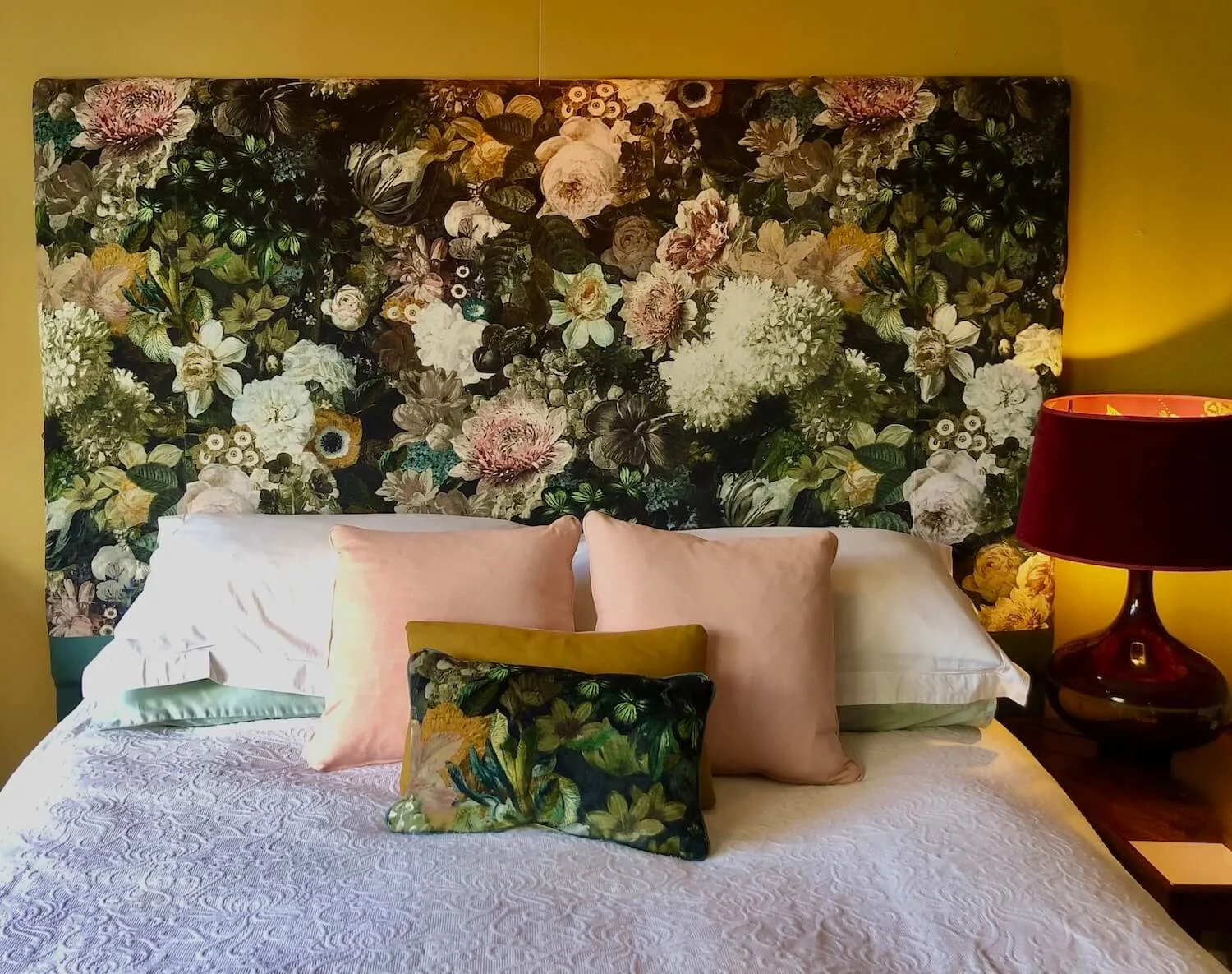 Floral upholstered headboard styled with sage green and pink cushions