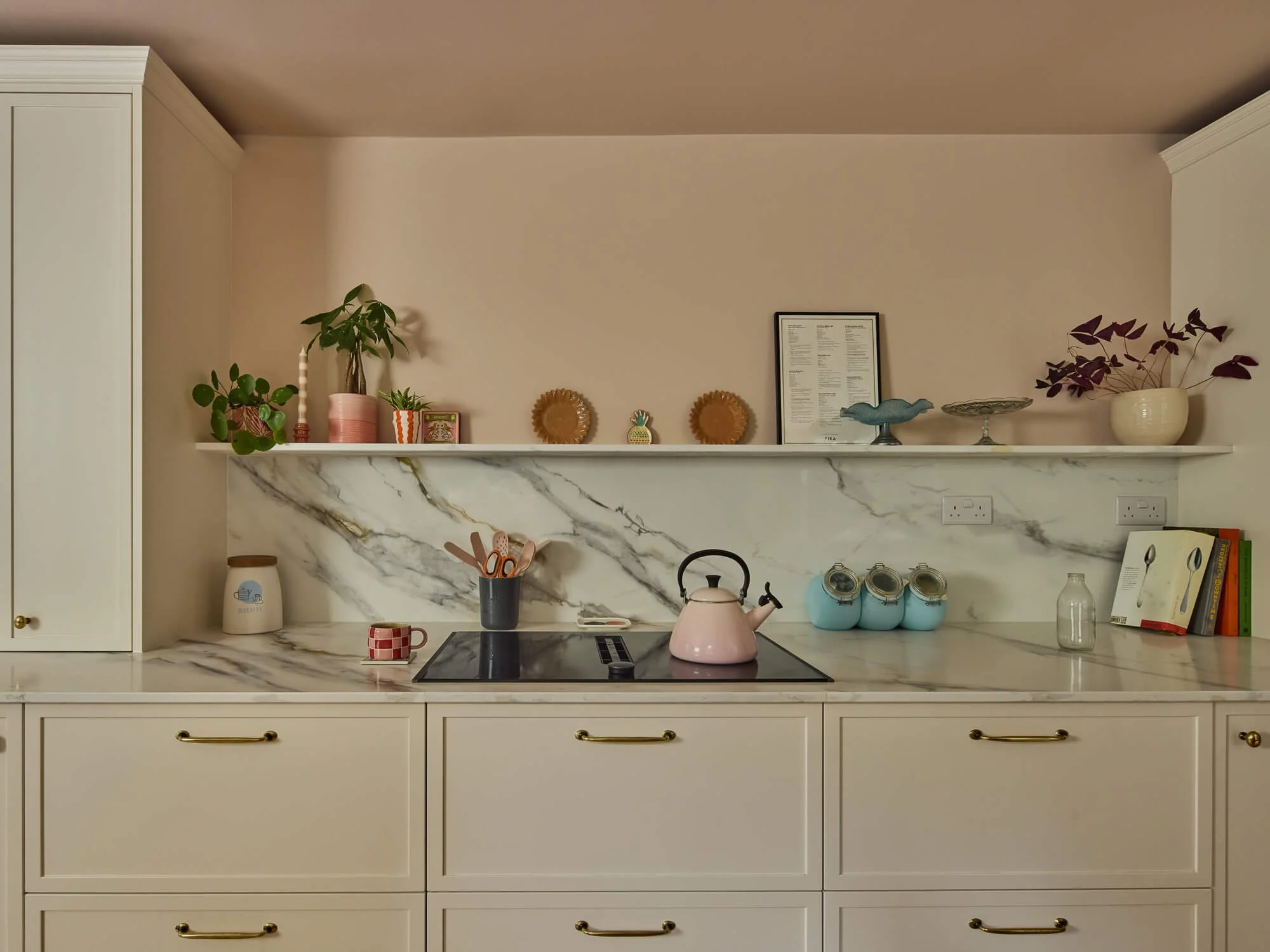 Elegant kitchen with marble splashback, blush walls, brass hardware, styled shelving.