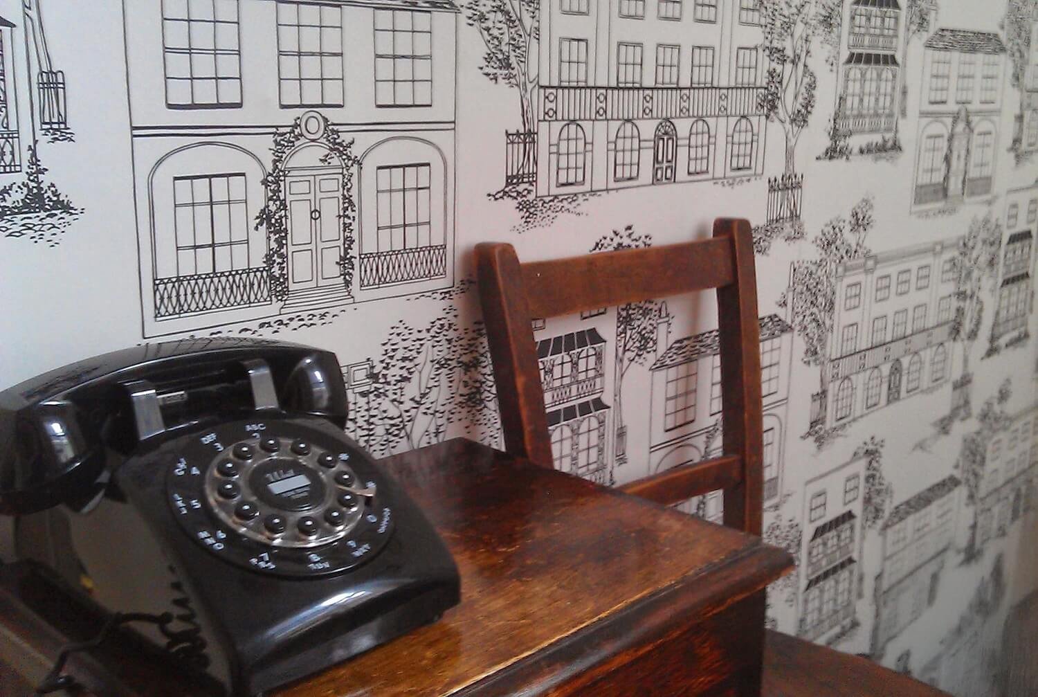 Vintage telephone on small wooden desk against illustrated wallpaper