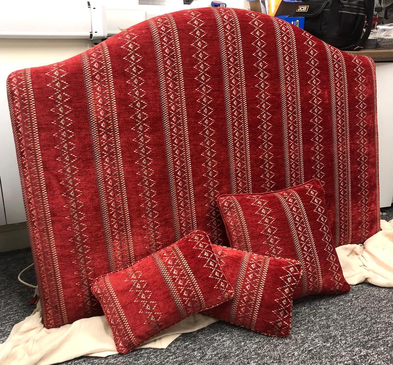 Red patterned upholstered headboard with matching bolster cushions