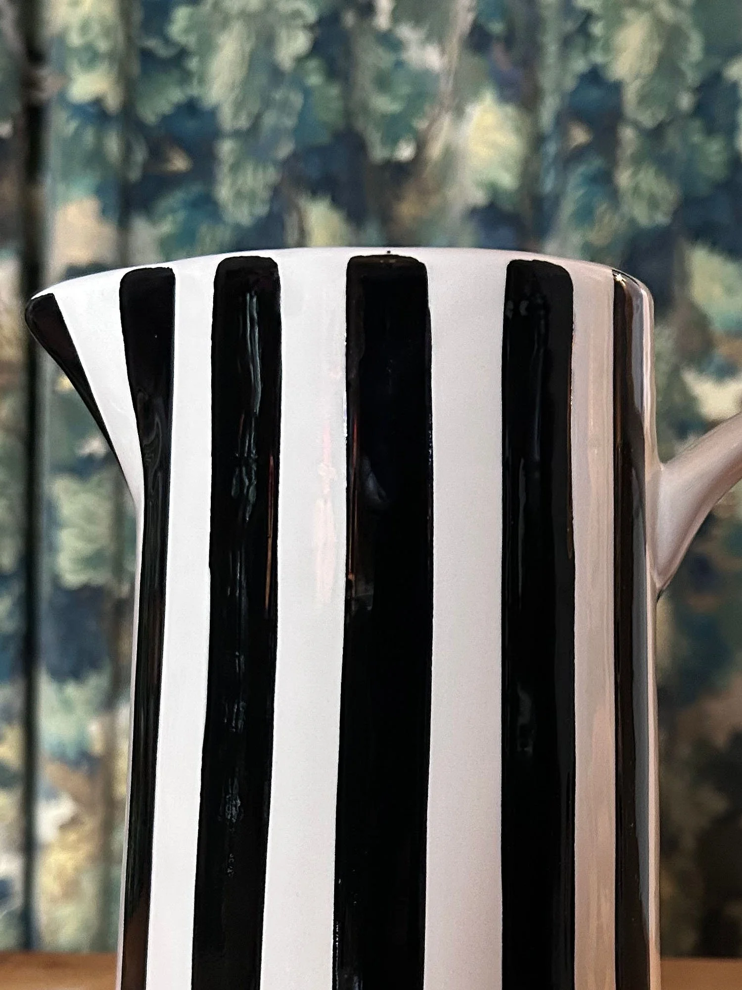 Black and white striped jug with side handle against patterned backdrop
