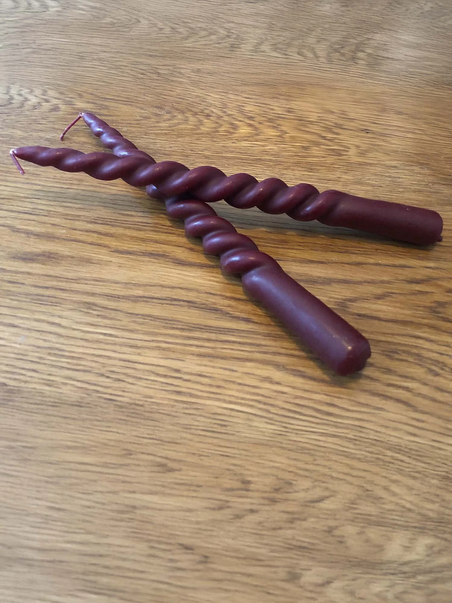 Pair of burgundy twisted candles on wooden surface