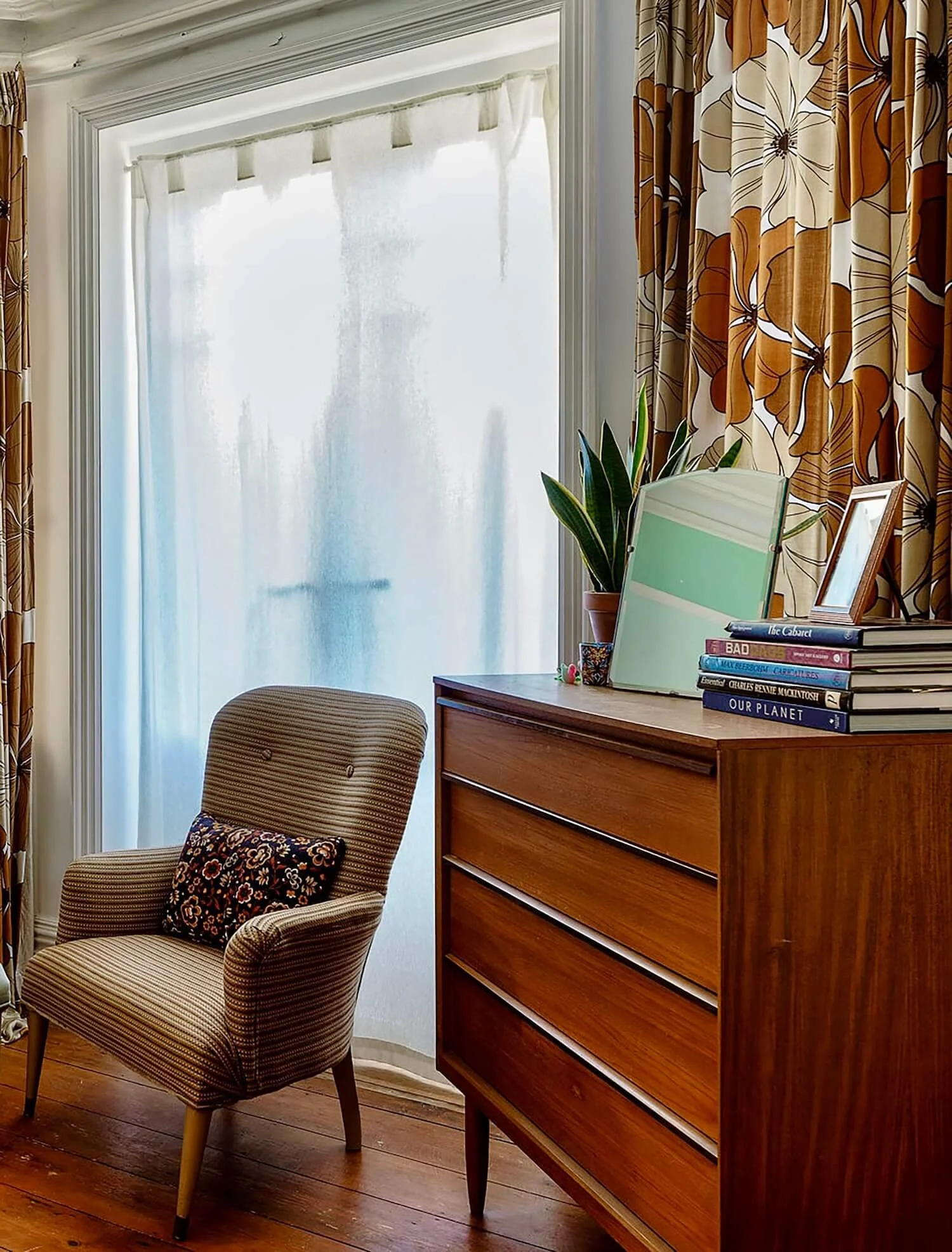 French doors with sheer curtains beside mid-century chest of drawers and armchair