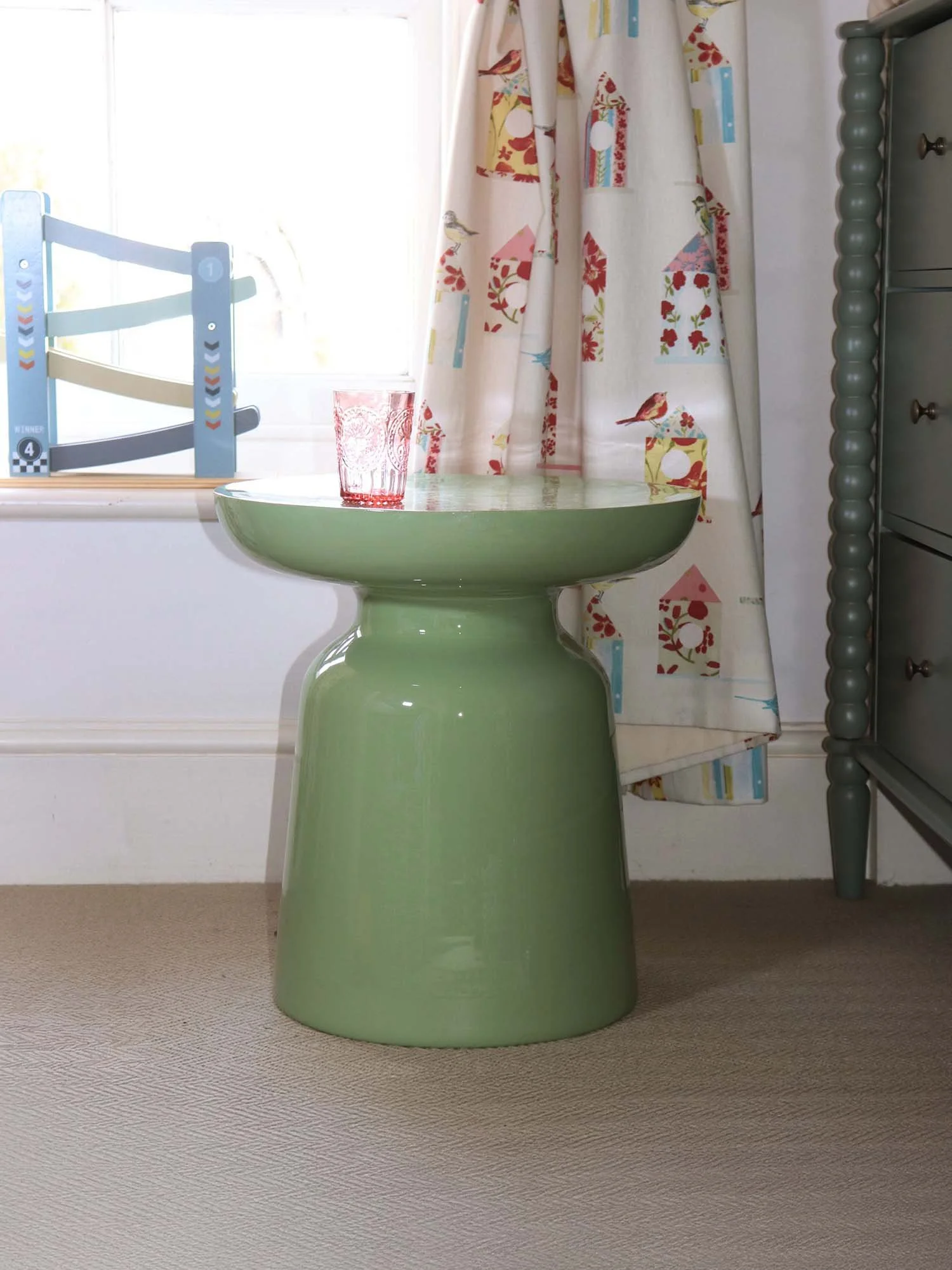Matcha green side table beside window with floral patterned curtains