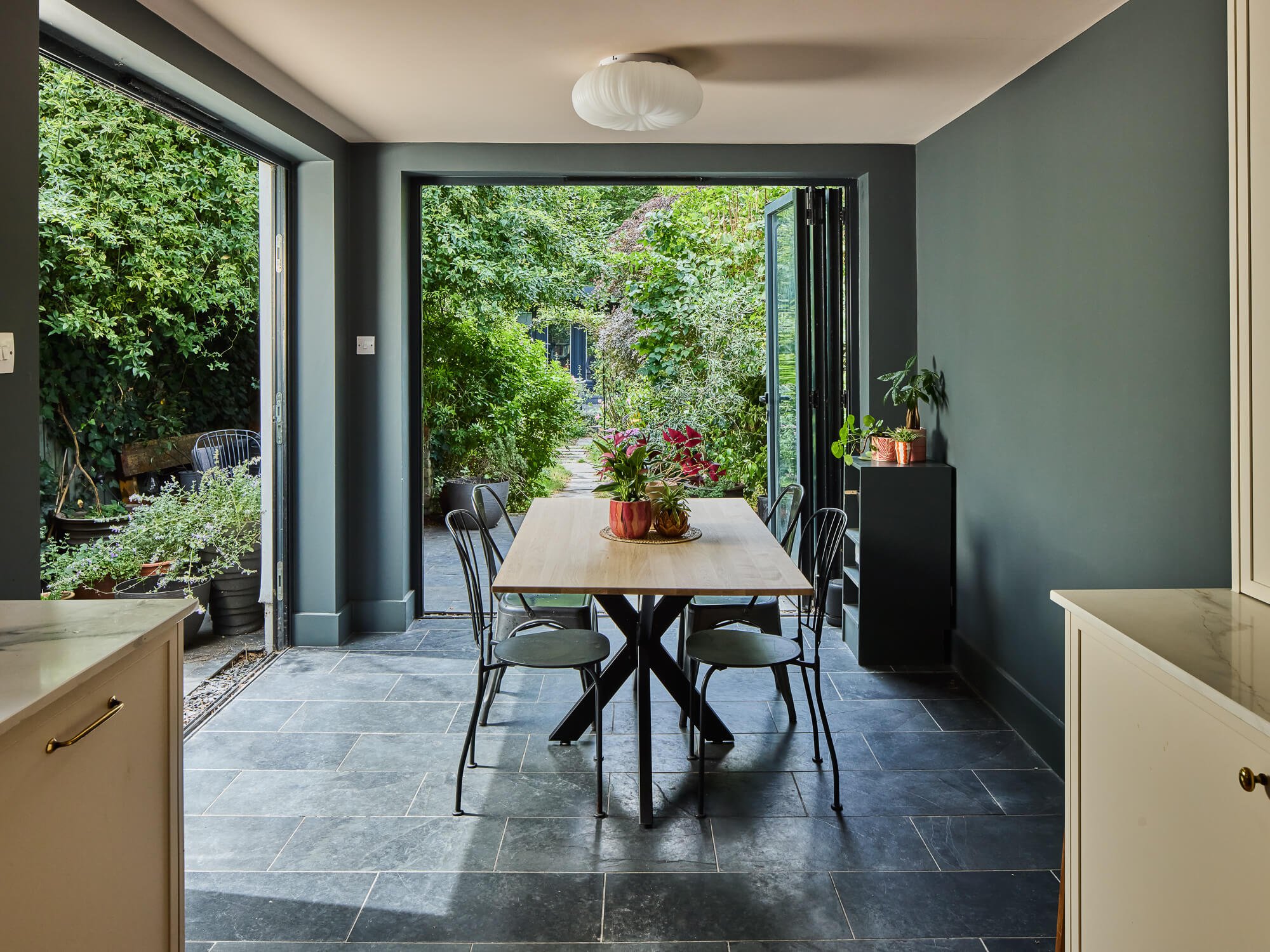 Modern dining space with garden views, blue walls, bifold doors.