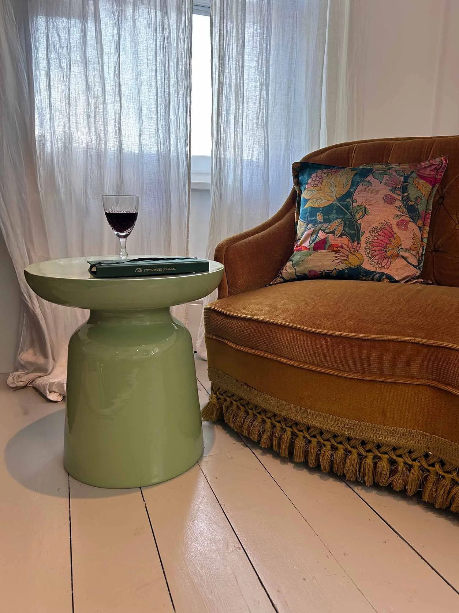 Matcha green side table with wine glass beside mustard armchair near window