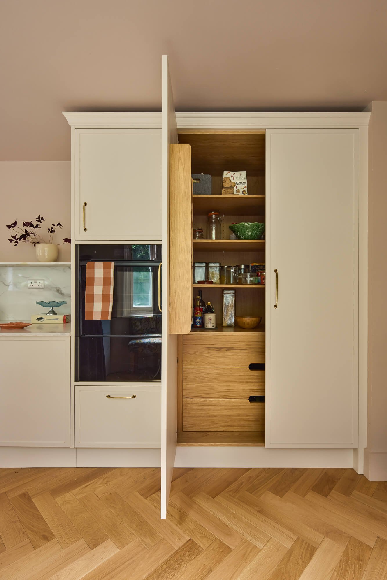 Bespoke kitchen pantry with oak interior, integrated storage, blush walls, herringbone flooring.