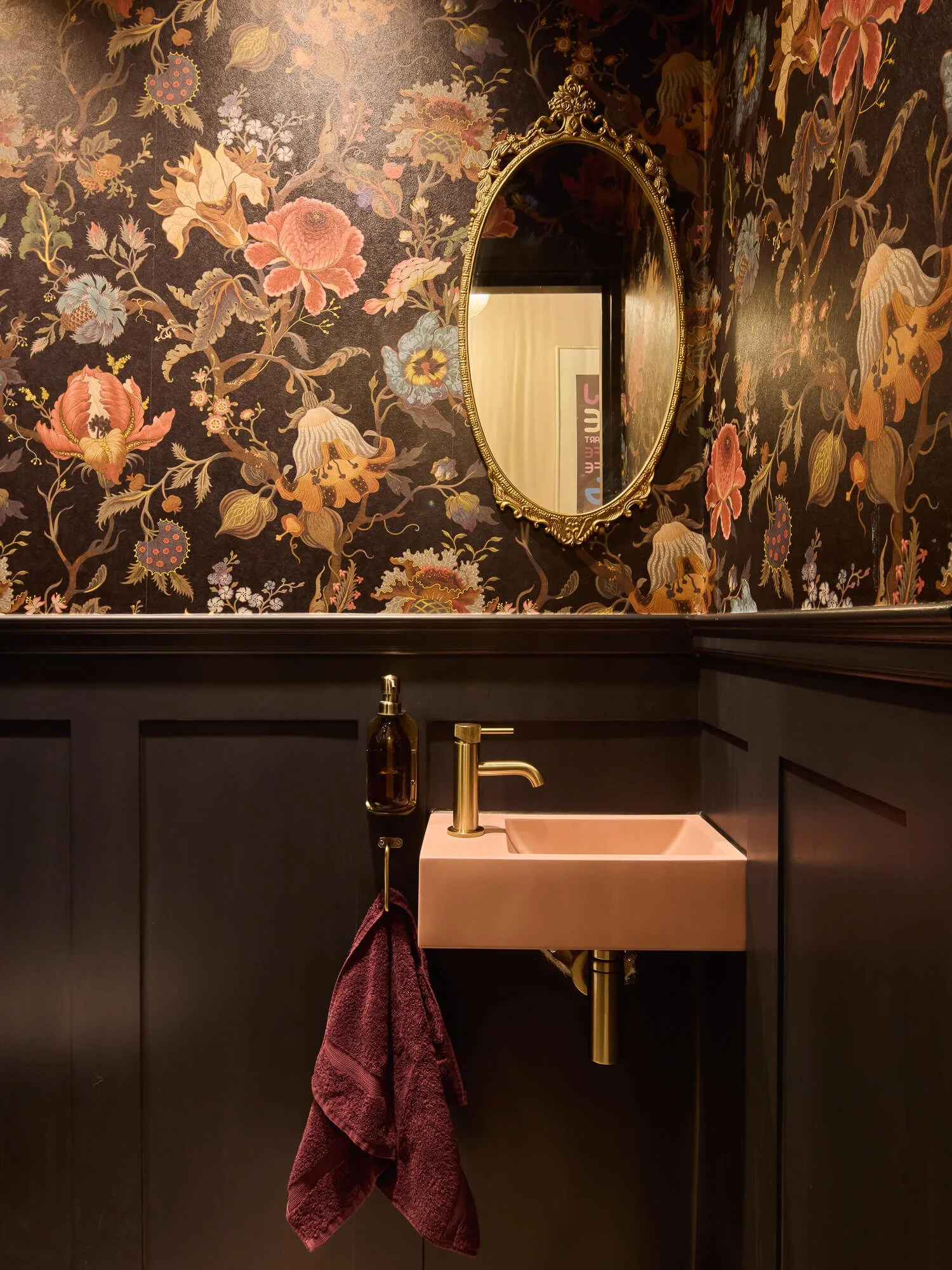 Elegant cloakroom with floral wallpaper, brass tap, pink basin, mirror.