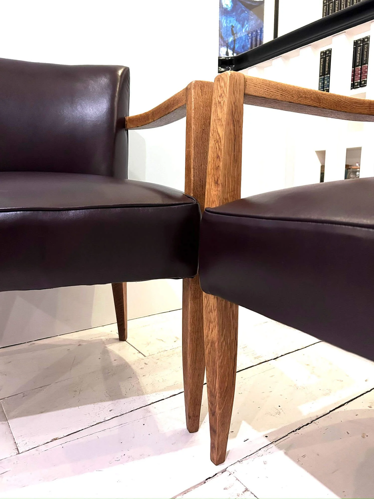 Close up of the oak tapered legs on two brown leather bridge chairs
