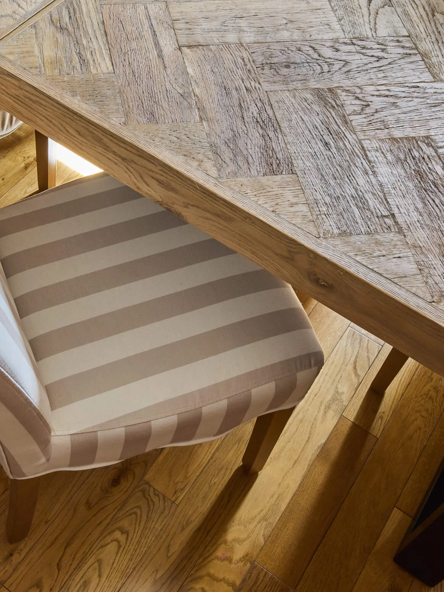 Close-up of oak dining table and striped upholstered dining chair detail.