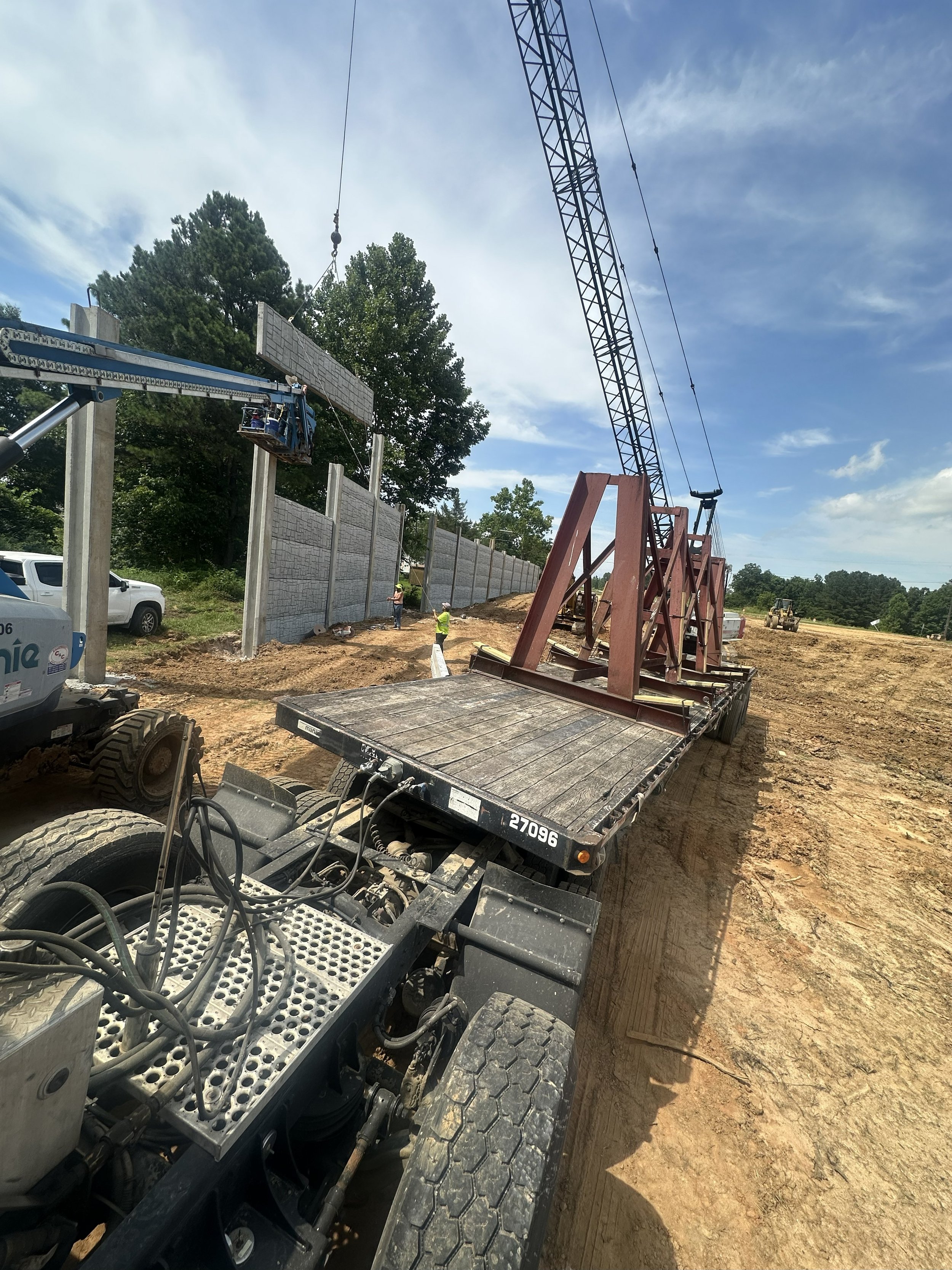 Construction site with a crane lifting a large concrete slab, workers in safety vests, and a partially built wall.