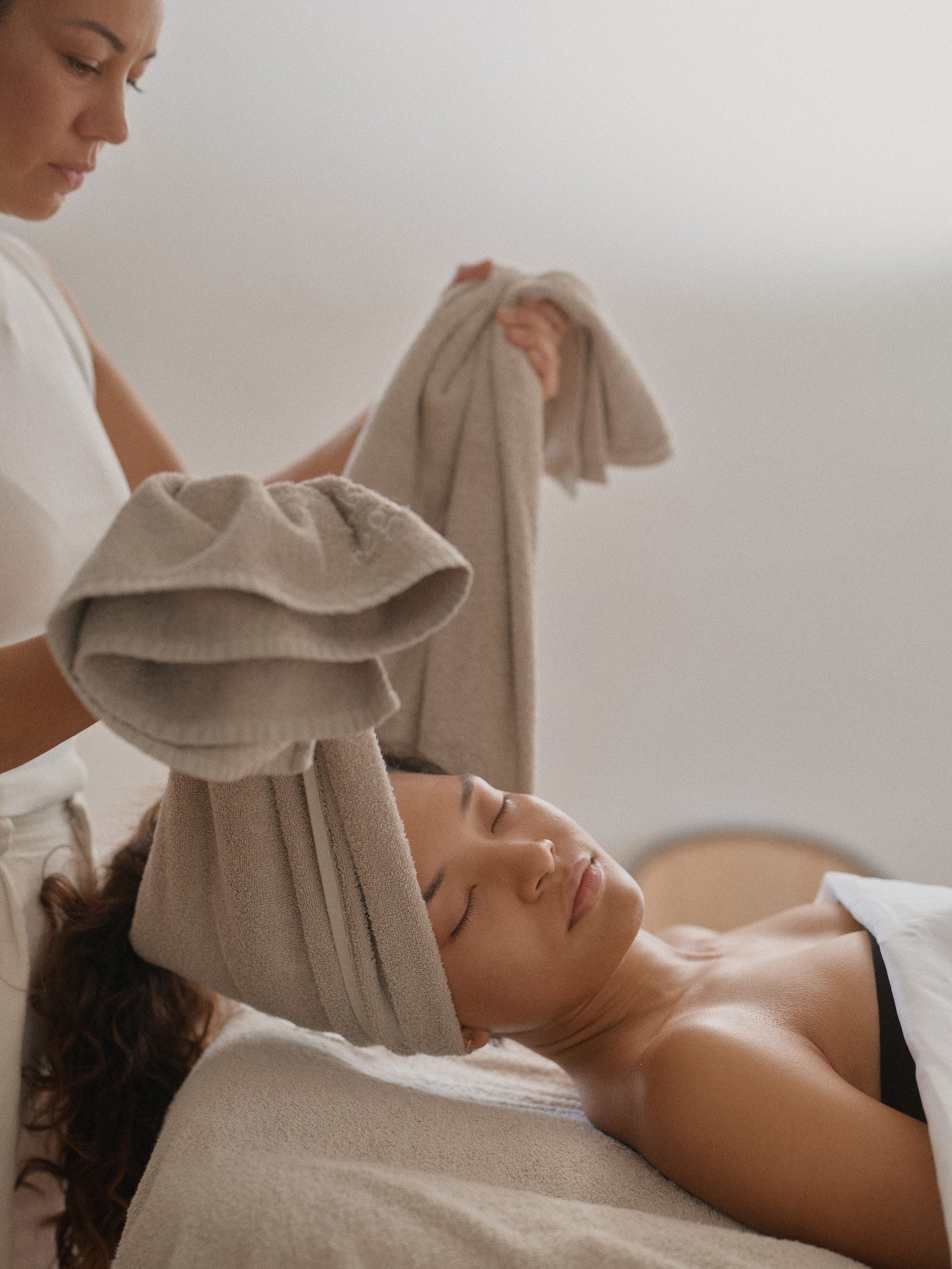 Das Model Helen Ferreira wird von Lena Carrera behandelt und in diesem Bild mit einem Handtuch unter dem Nacken und Kopf sanft von dem Behandlungsbett hochgehoben, sodass ihr Nacken entspannt und gedehnt wird.