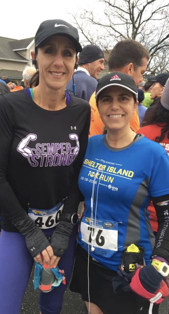 Two women dressed in running gear, smiling and standing close together at a marathon event, surrounded by other runners and spectators.