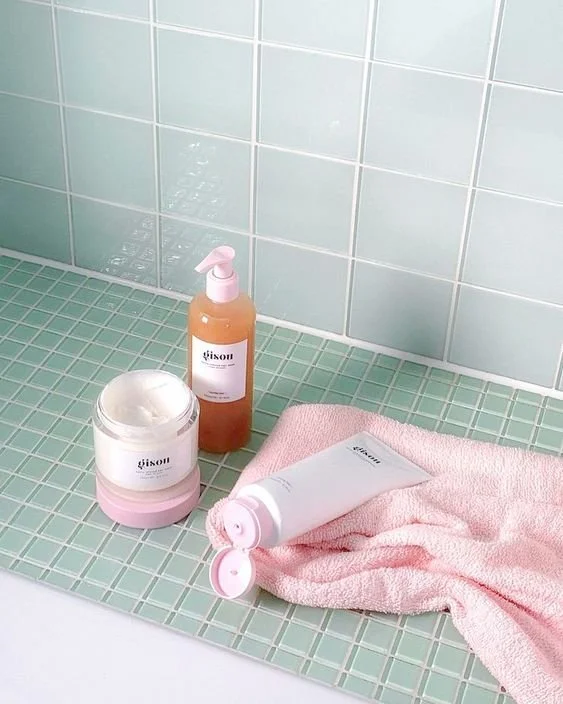 Bathroom countertop with pink towel, white jar, pink bottle, and white tube, all labeled with brand Gison, against light green tiled wall.