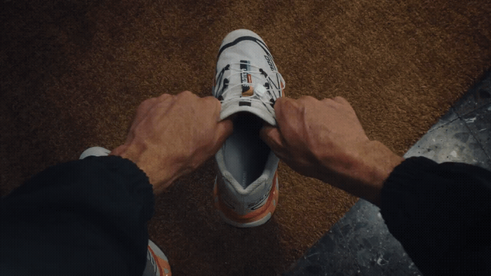 Person tying their running shoes in an indoor setting with a brown carpeted floor.
