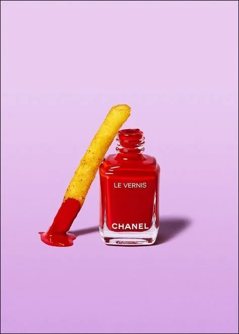 A nail polish bottle with red polish and a French fry dipped in red nail polish leaning against it.