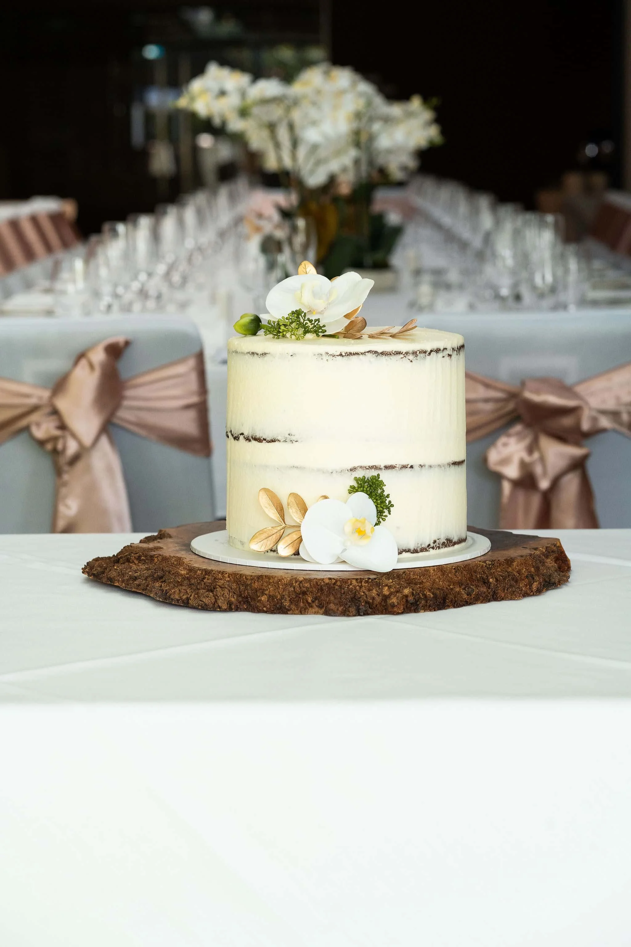 A white wedding cake with floral decorations on a wooden cake stand at a reception table.