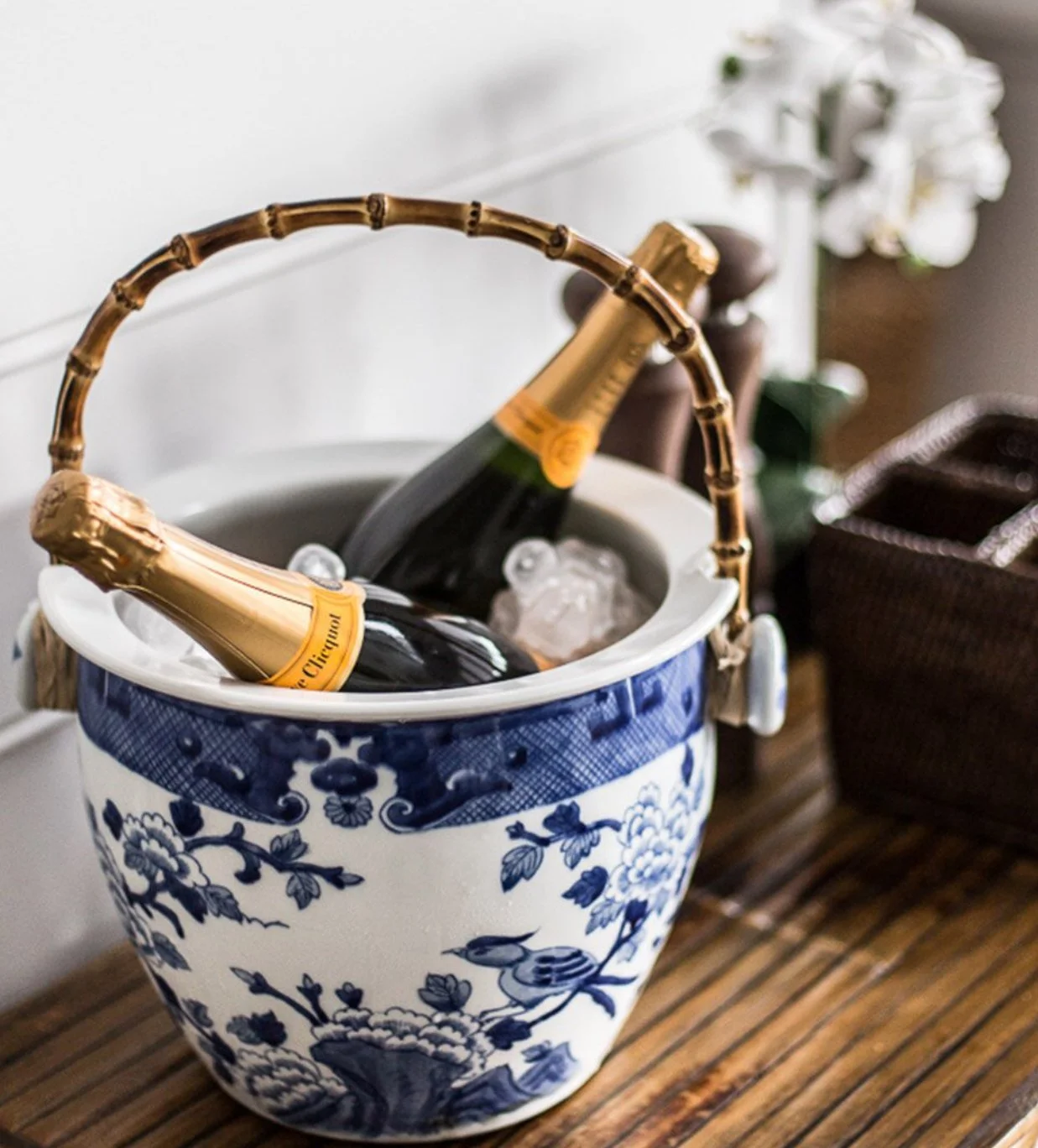 Two bottles of champagne in an ice bucket with ice, placed on a wooden surface, with a floral arrangement in the background.
