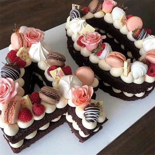 Chocolate cake decorated with pink roses, macarons, raspberries, and white and pink meringues, arranged in the shape of the number 30.