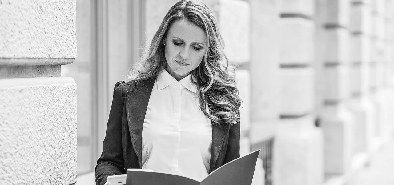 Black and white photo of Dora in business attire reading a document outdoors.
