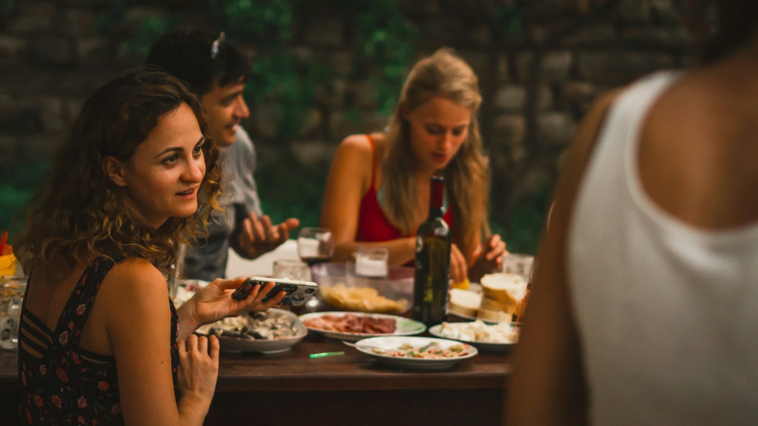 Group of friends having dinner outdoors, with plates of food and drinks on the table.
