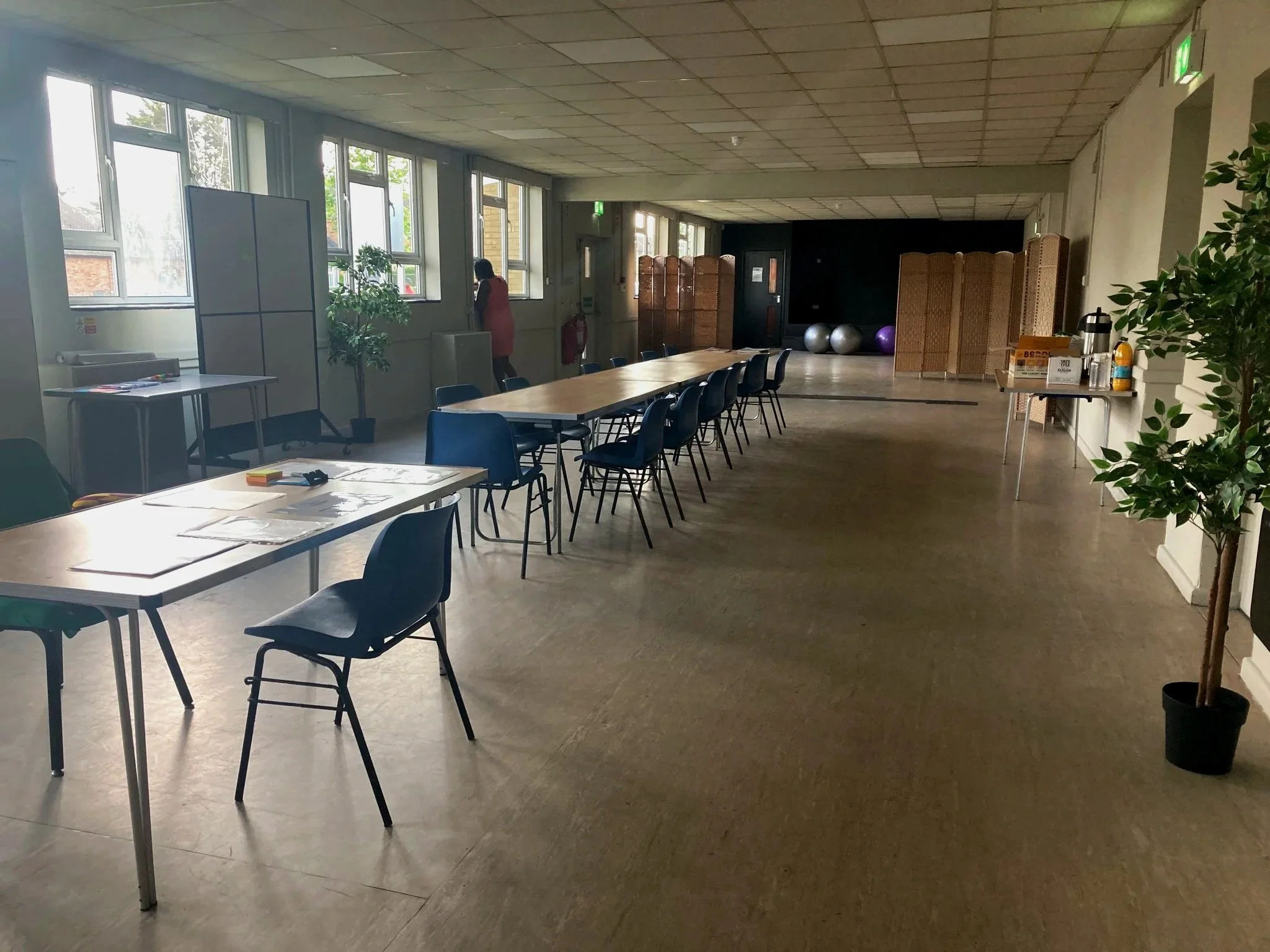 Long conference room with tables and chairs, large windows, and a small refreshment table with coffee and snacks.