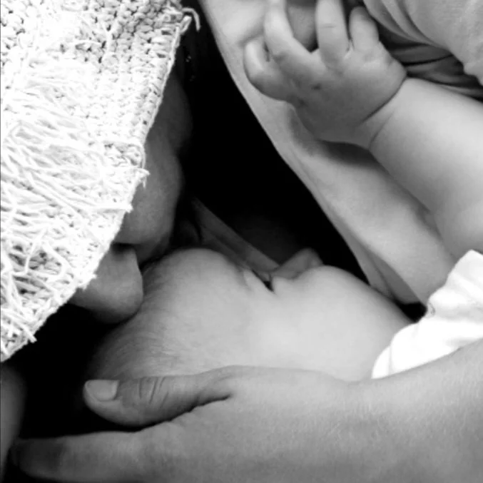 A baby is held by a person cloaked in a blanket