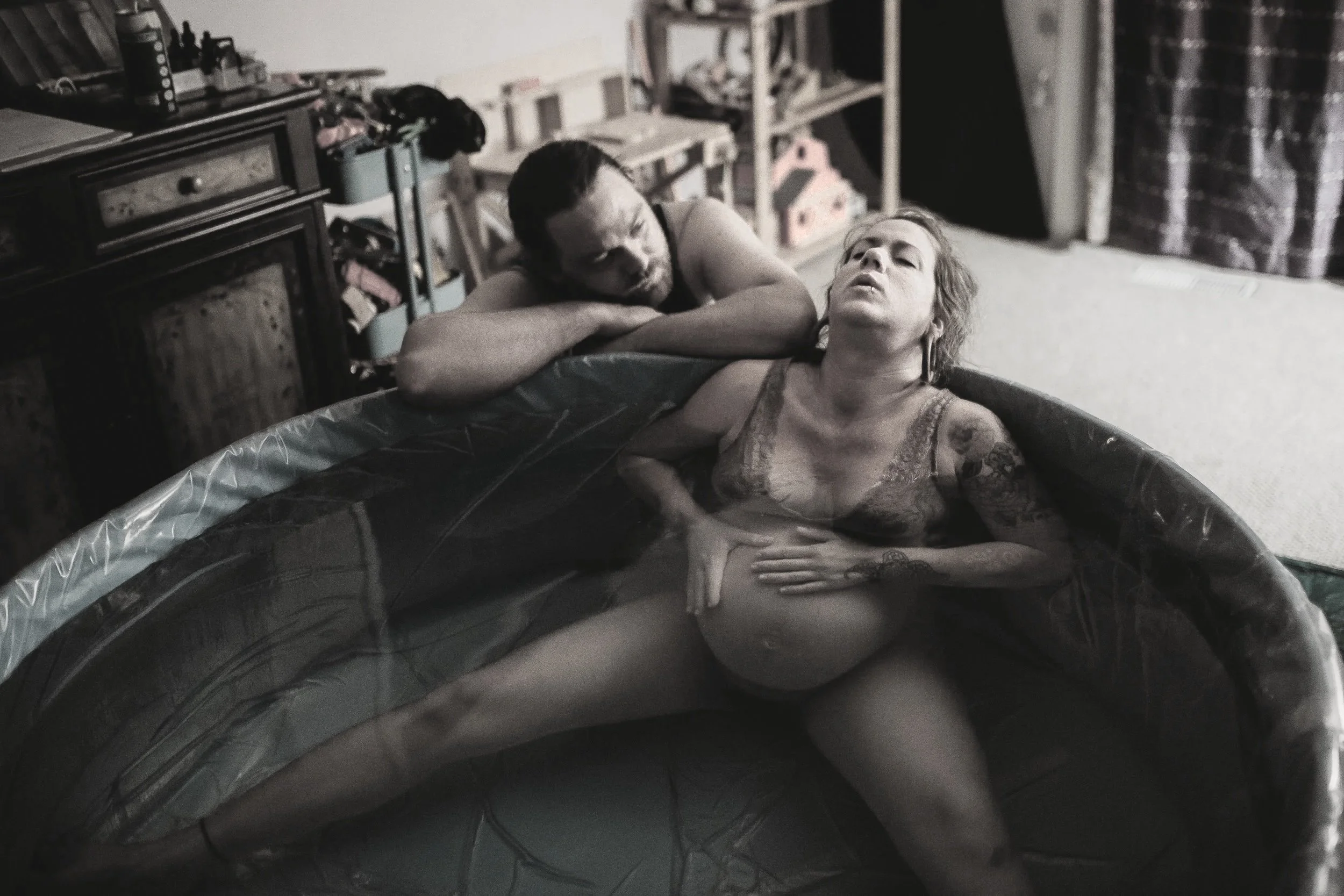A woman sits back against the edge of a birthpool while a partner sits behind her