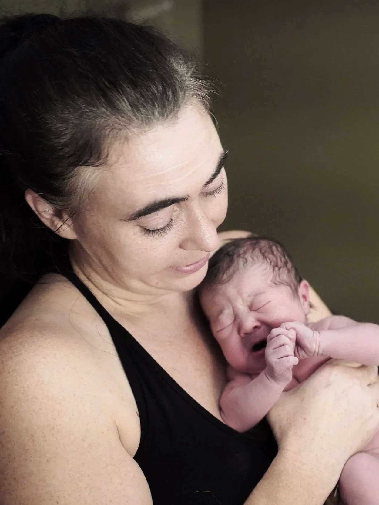 A woman holding a newborn baby close to her chest, with both of them appearing to be crying or upset.