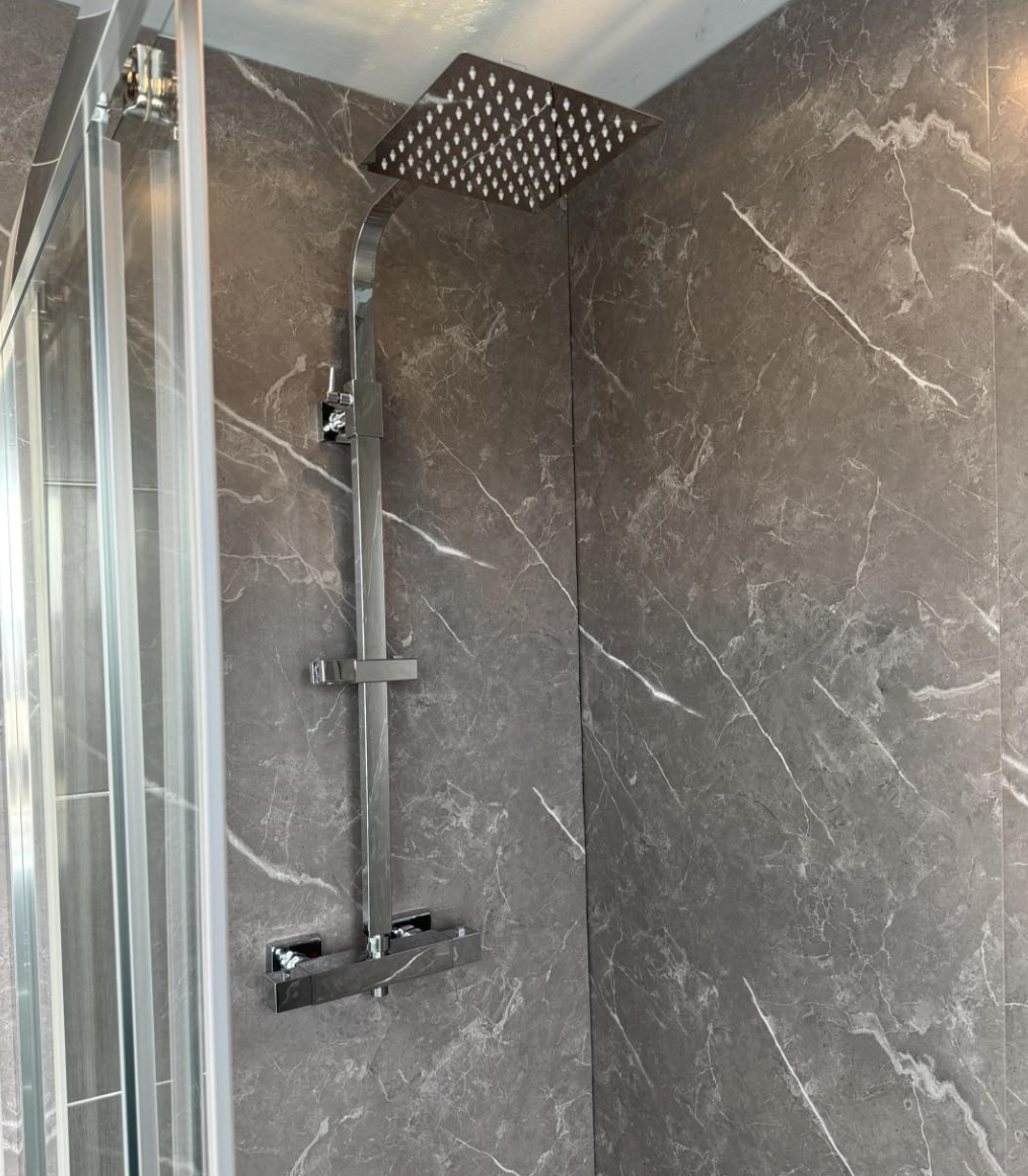 Modern shower with large square rainfall showerhead, dark gray marble walls, and a glass door.